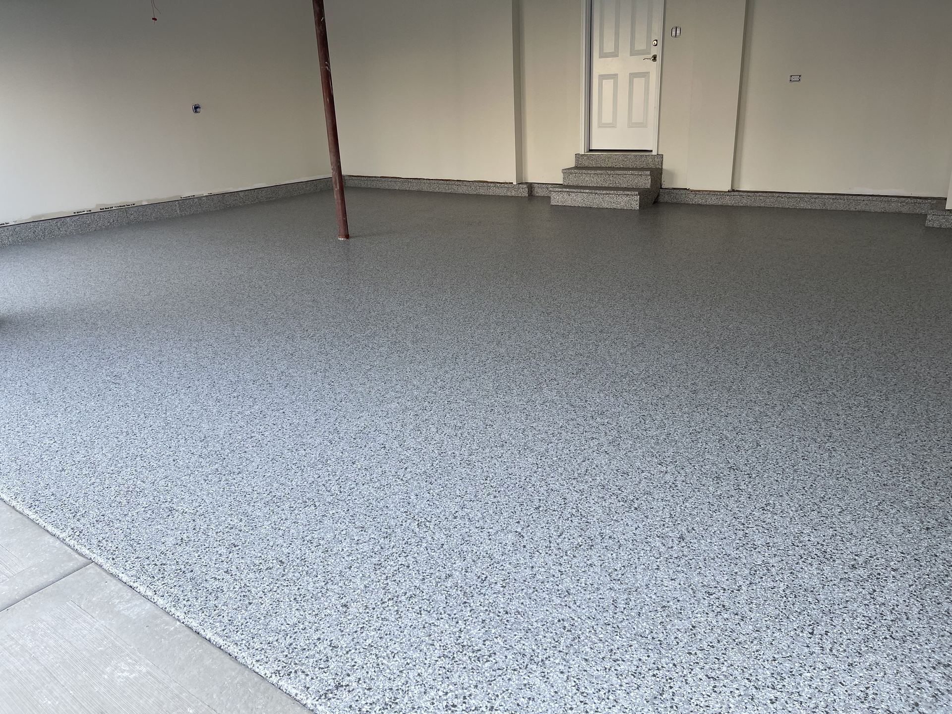 Empty garage with clean, speckled epoxy flake floor and a door with steps at the back wall.