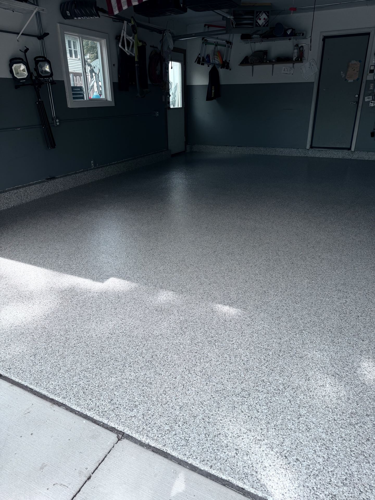 Clean, newly finished epoxy flake garage floor with gray walls and organized tools on shelves.