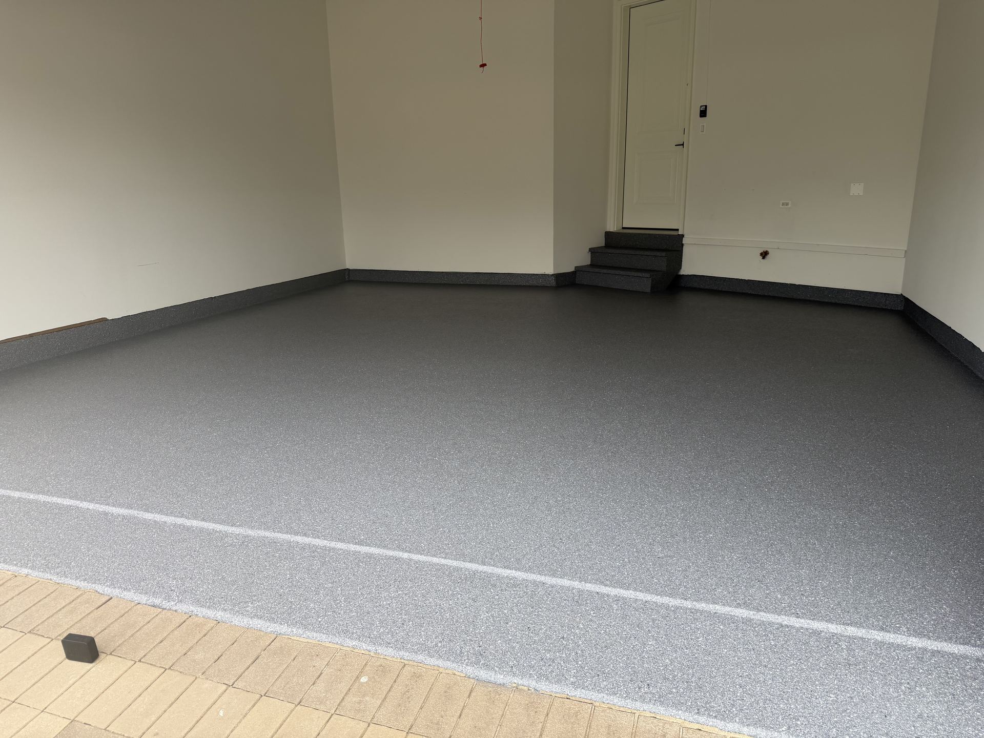 Clean gray epoxy flake garage floor with low steps leading to a white door inside a neutral-colored garage.