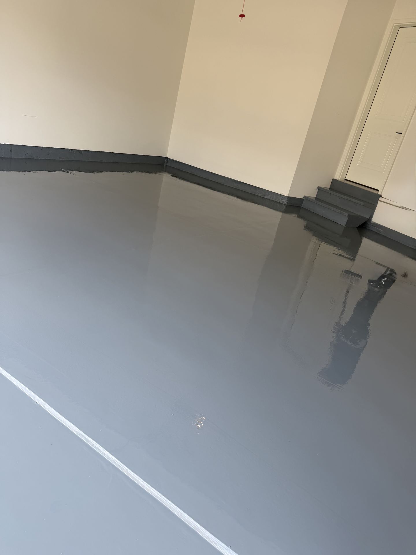 Empty garage with newly coated smooth gray epoxy floor and gray trim along white walls.