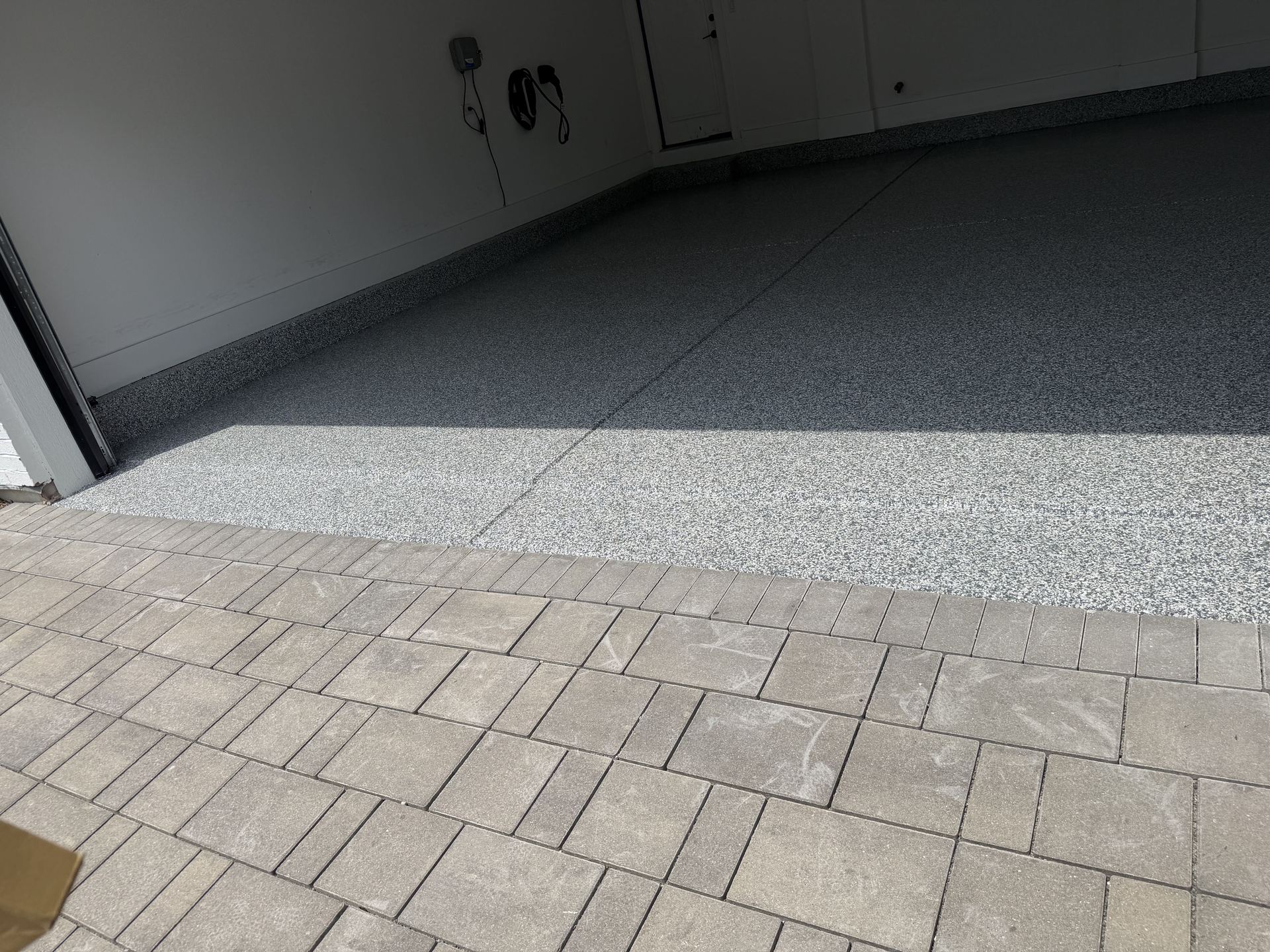 Epoxy flake coated garage floor transitioning to a paved driveway with gray rectangular bricks.