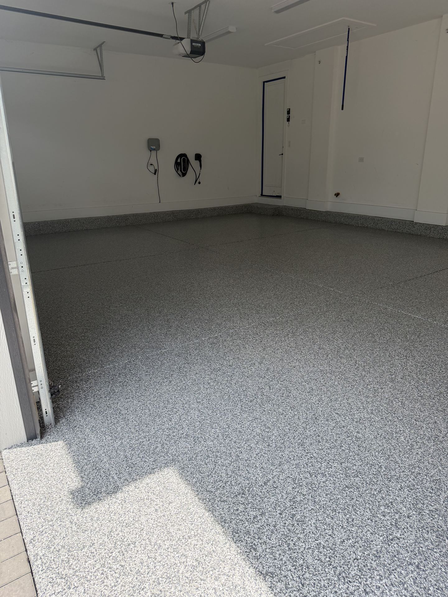 Clean, empty garage with newly installed gray epoxy flake flooring and white walls.