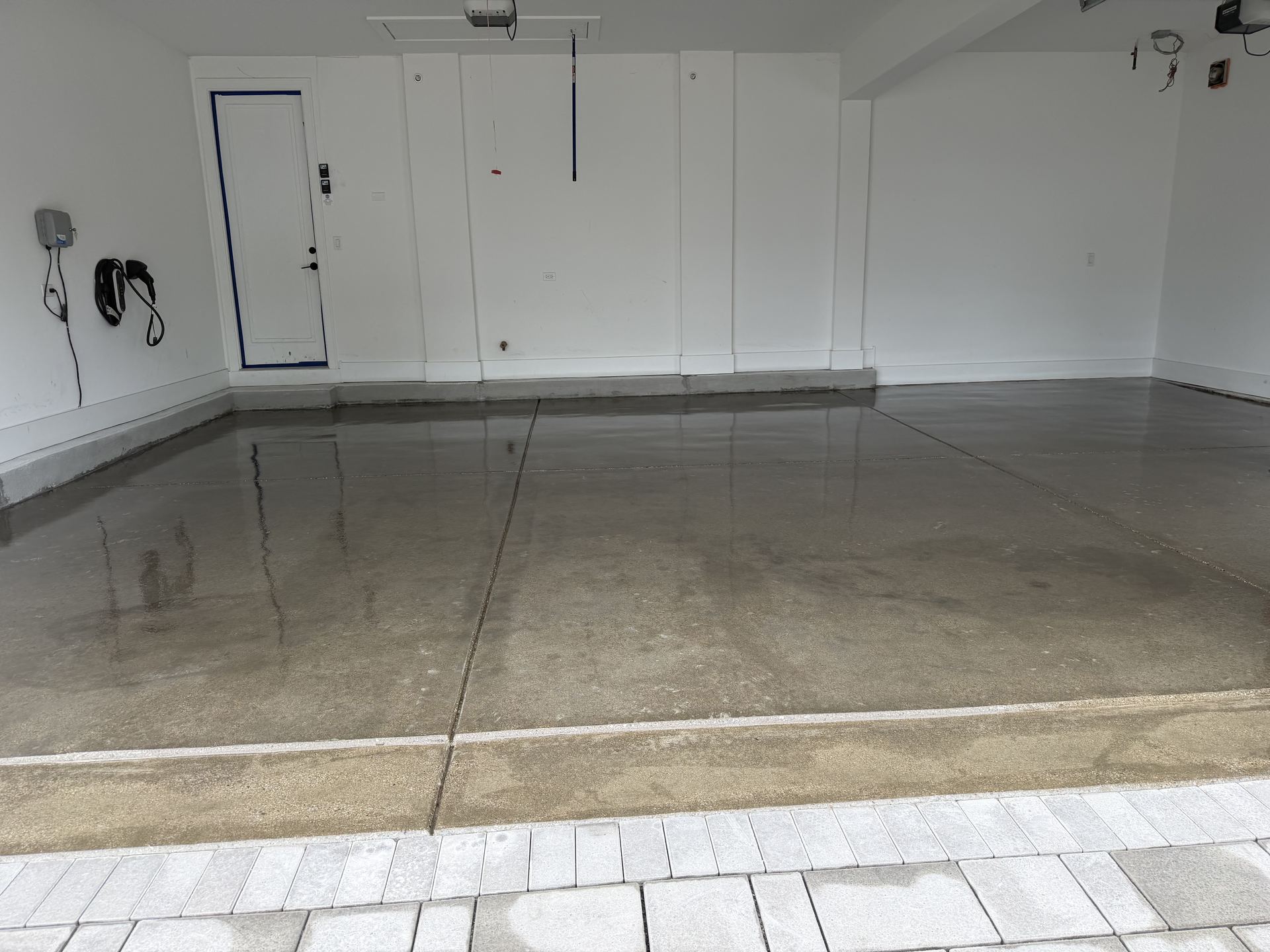 Empty garage with polished concrete floor, white walls, and a closed door on the left.