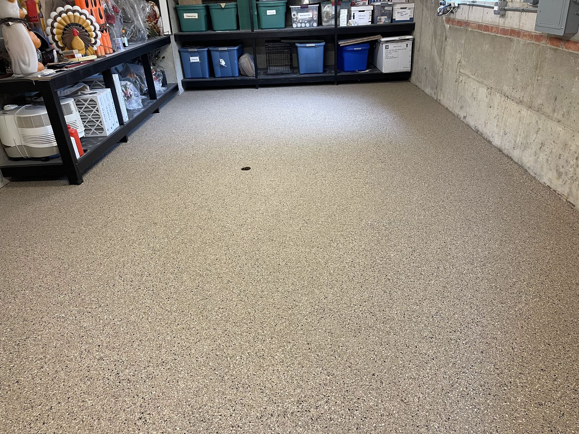 Basement storage area with newly finished light speckled epoxy flake flooring and shelves with storage bins.