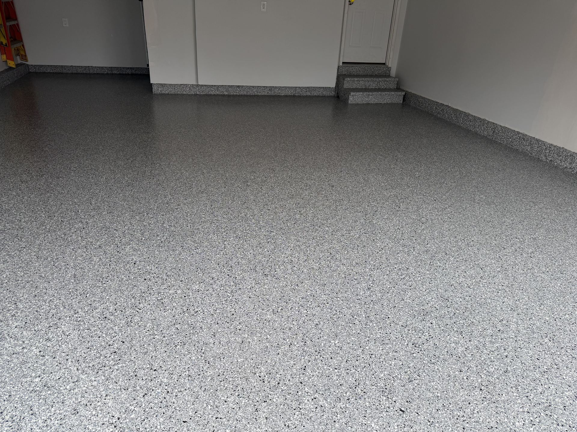 Clean garage floor with gray epoxy flake coating and matching base trim under white walls.