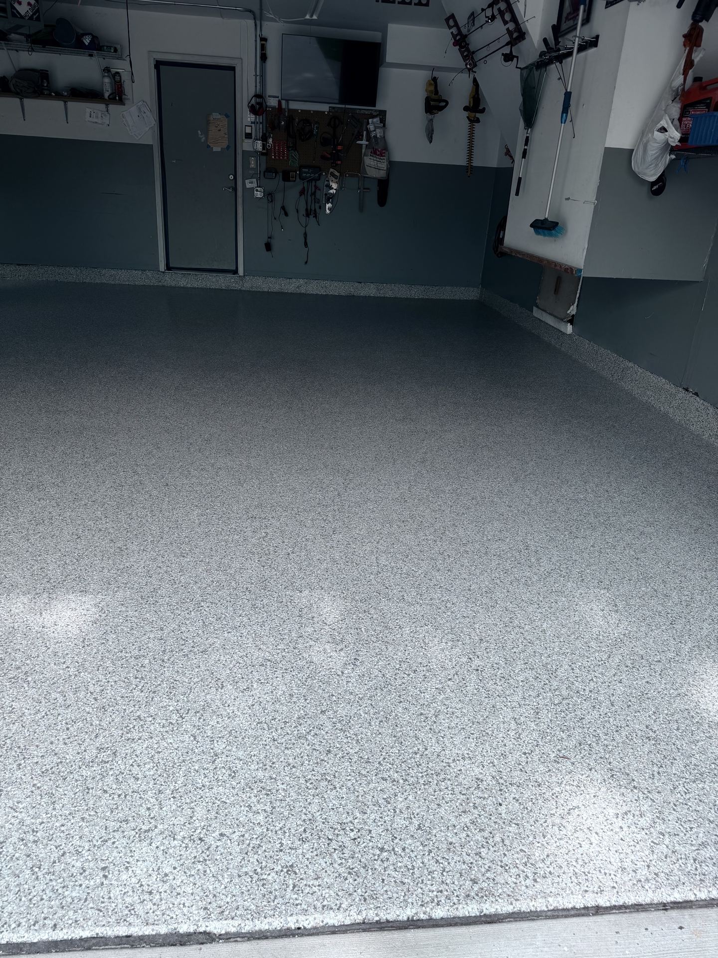 Clean garage interior showing a newly finished speckled epoxy floor and organized walls with tools.
