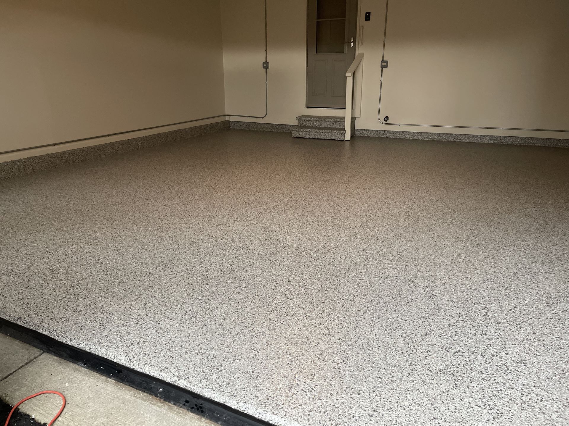 Clean garage interior with freshly finished epoxy flake floor and beige walls and door.