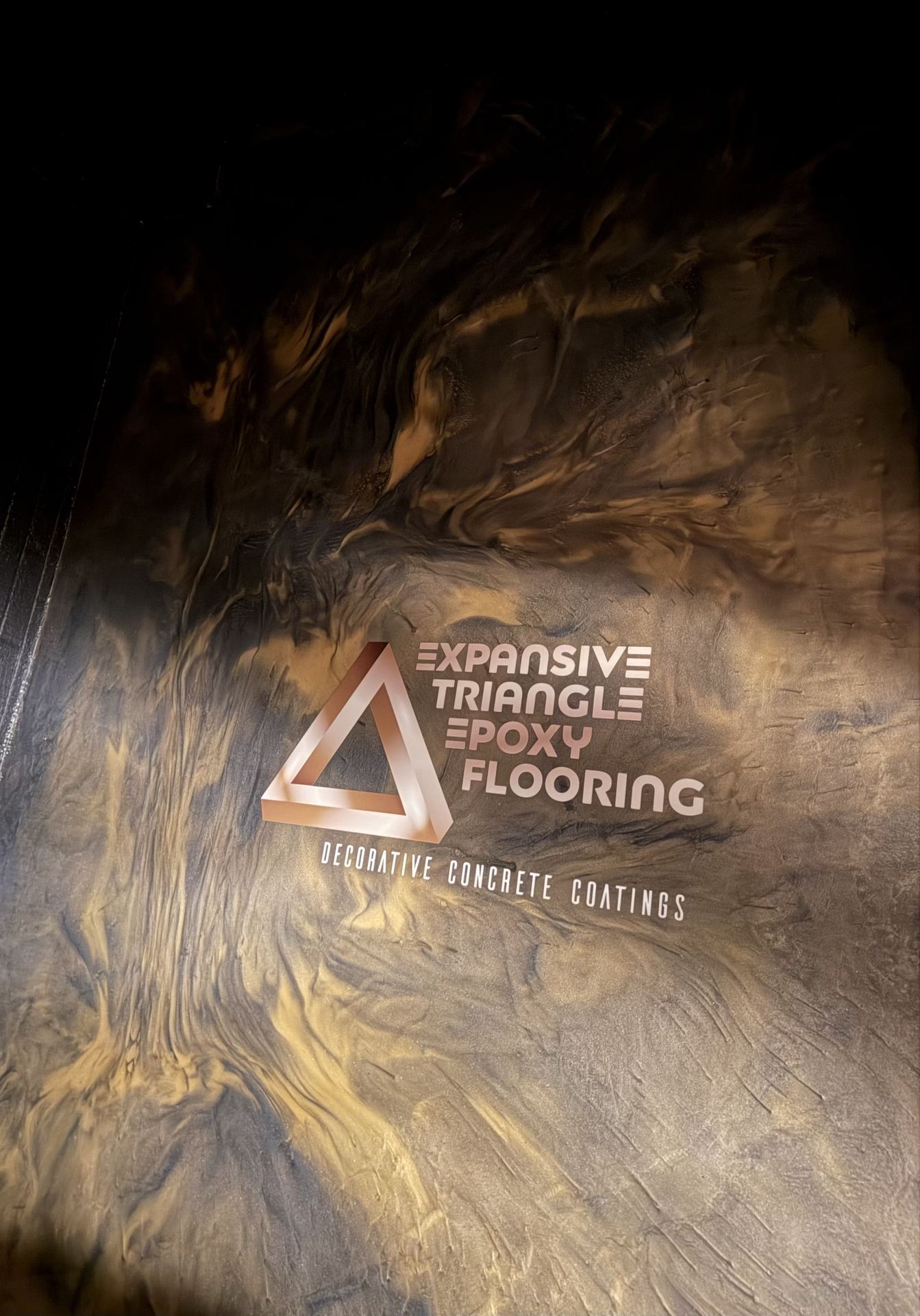 Metallic epoxy flooring with swirling gold and black colors and Expansive Triangle Epoxy Flooring logo.