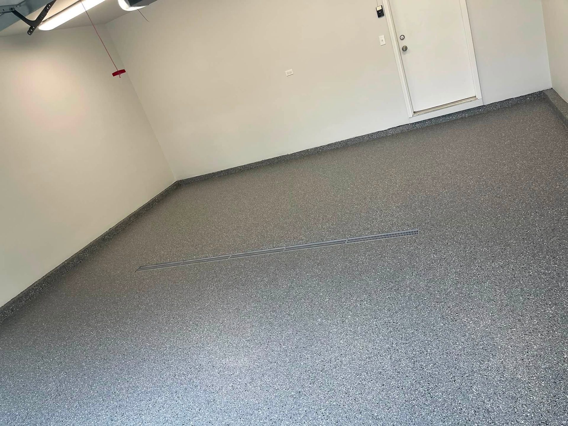 Smooth gray epoxy flake flooring with speckled texture in an empty room with white walls.