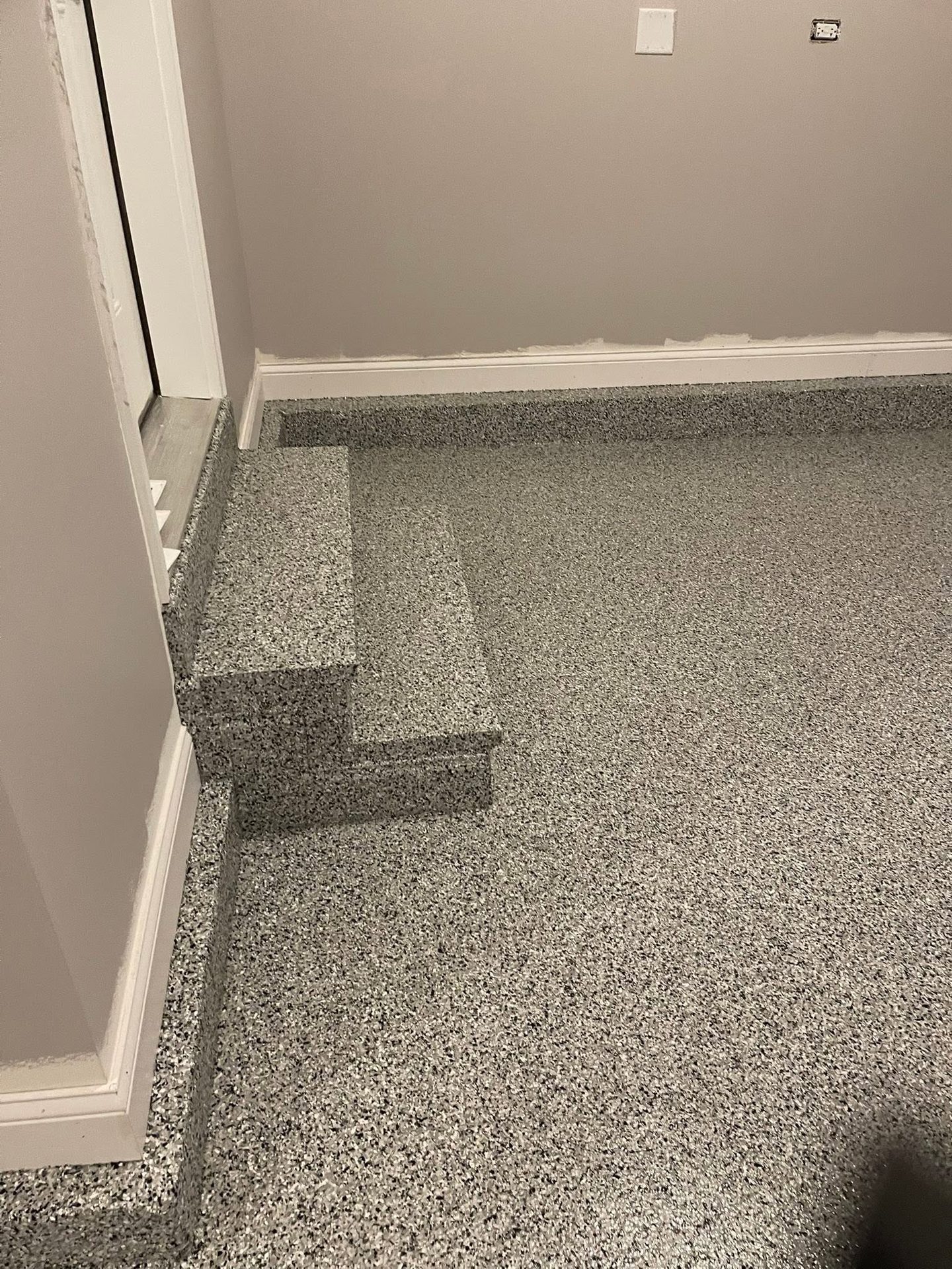 Grey speckled epoxy flake flooring with matching stairs and baseboard in a room.