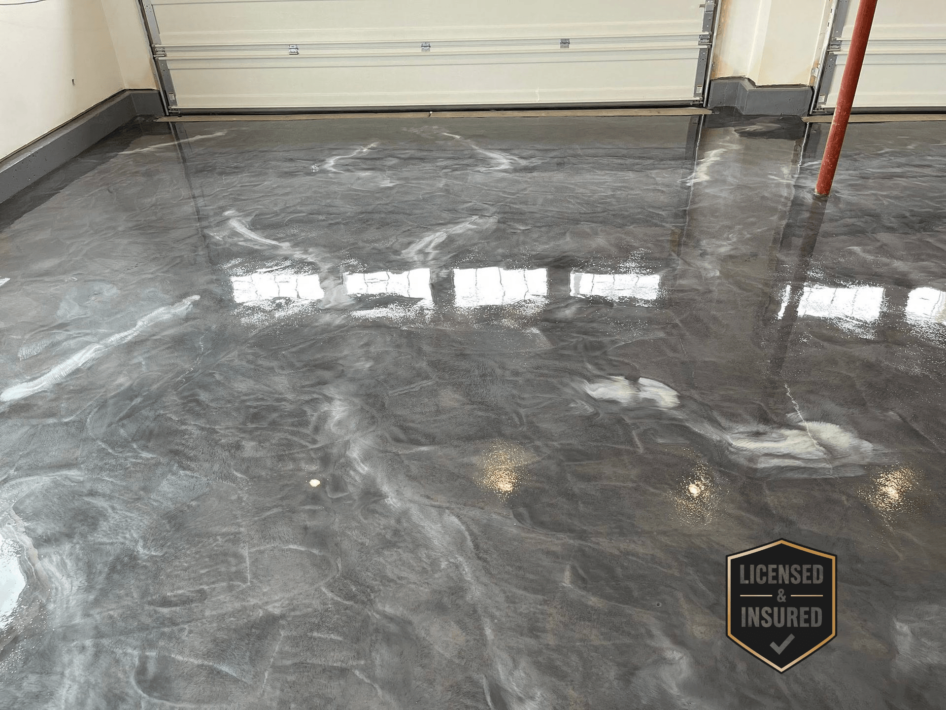 Glossy epoxy-coated garage floor with silver and gray swirls reflecting windows and ceiling lights.