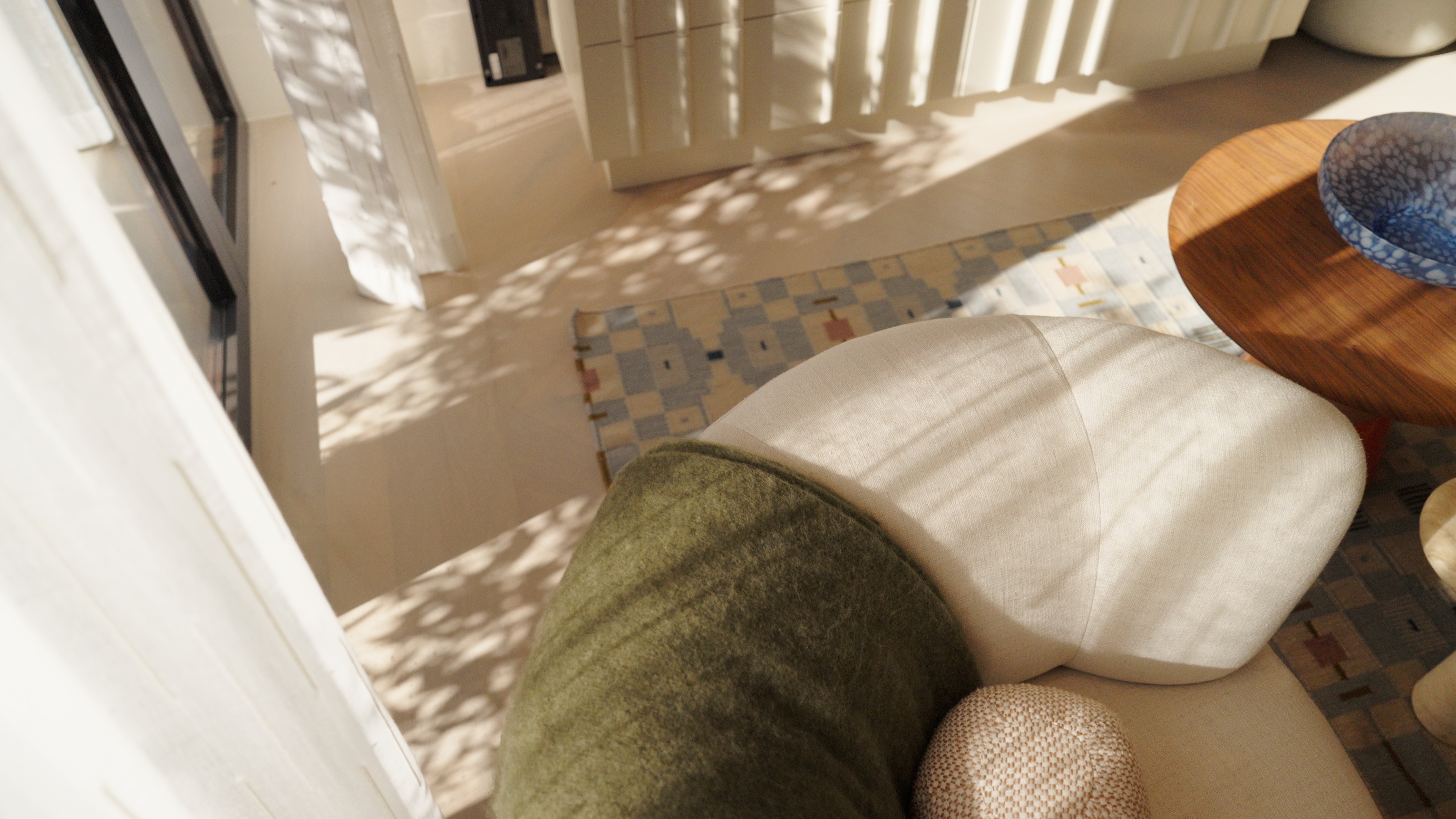 White cushioned chair with green and beige pillows near a wooden table with a blue bowl.