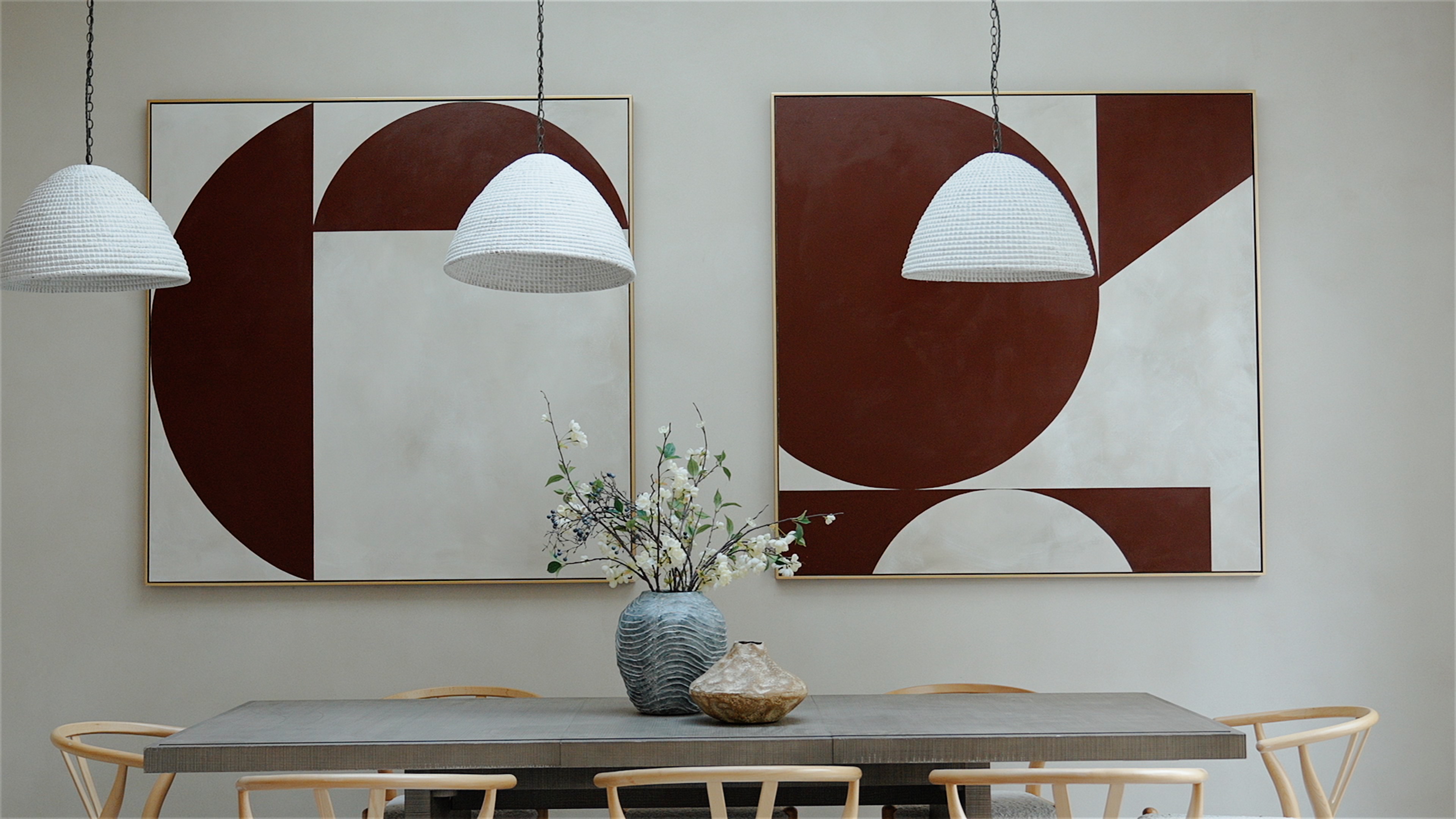 Minimalist dining room with gray table, wooden chairs, vase with flowers, and geometric wall art.