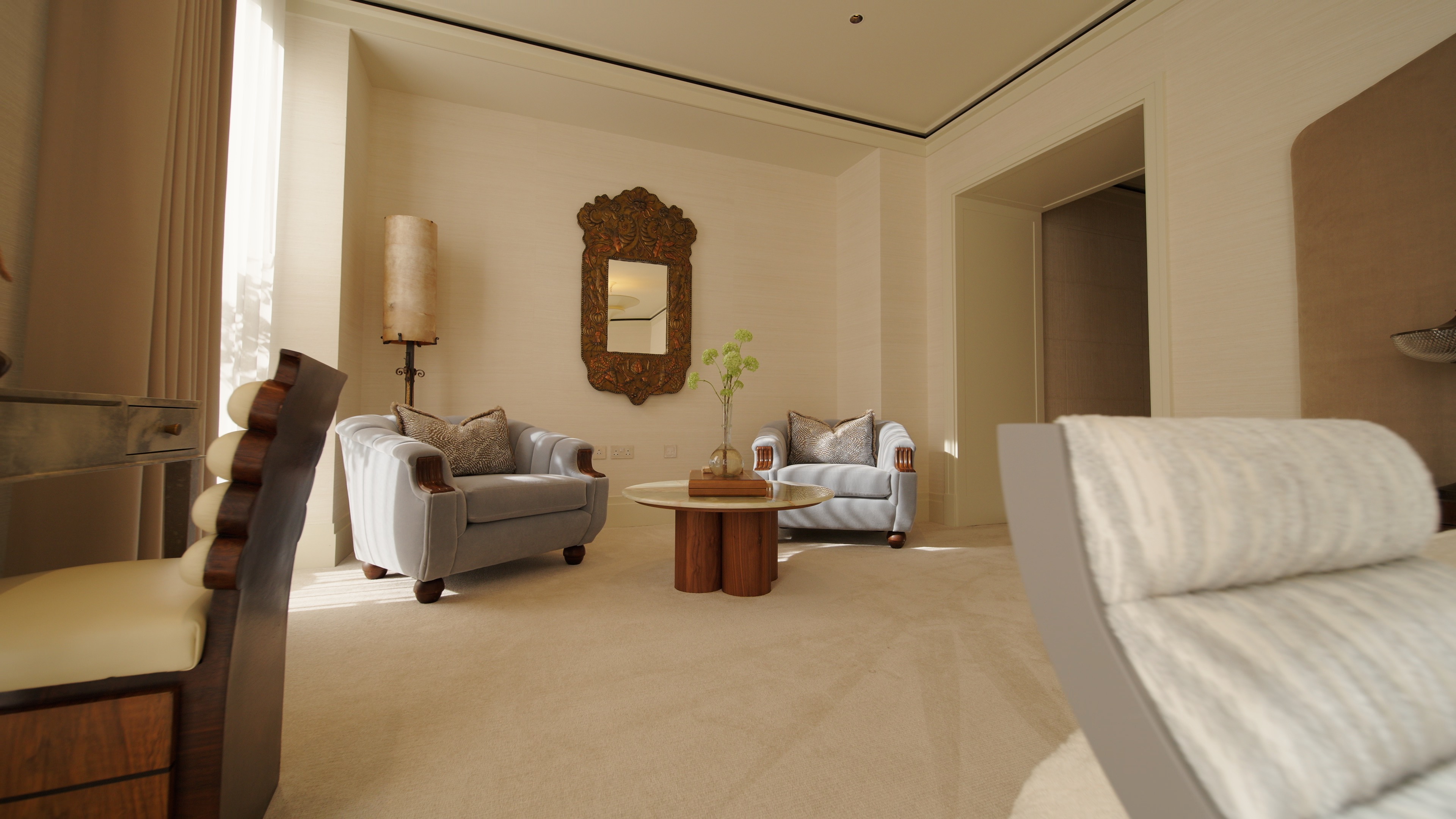 Two gray armchairs with patterned pillows next to a round wooden table and a decorative wall mirror.