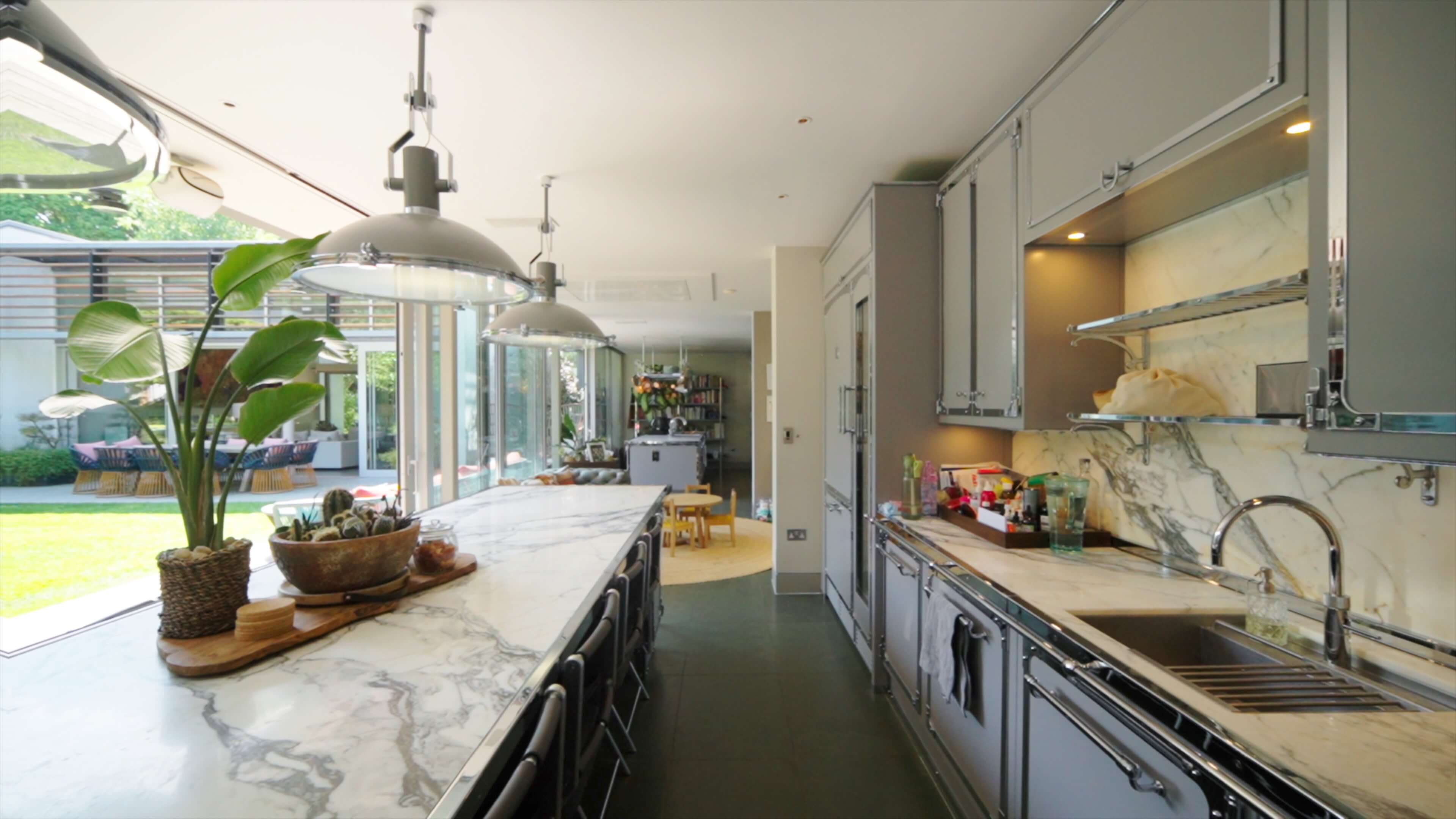 Modern kitchen with marble countertops, gray cabinets, pendant lights, and large windows overlooking a green yard.