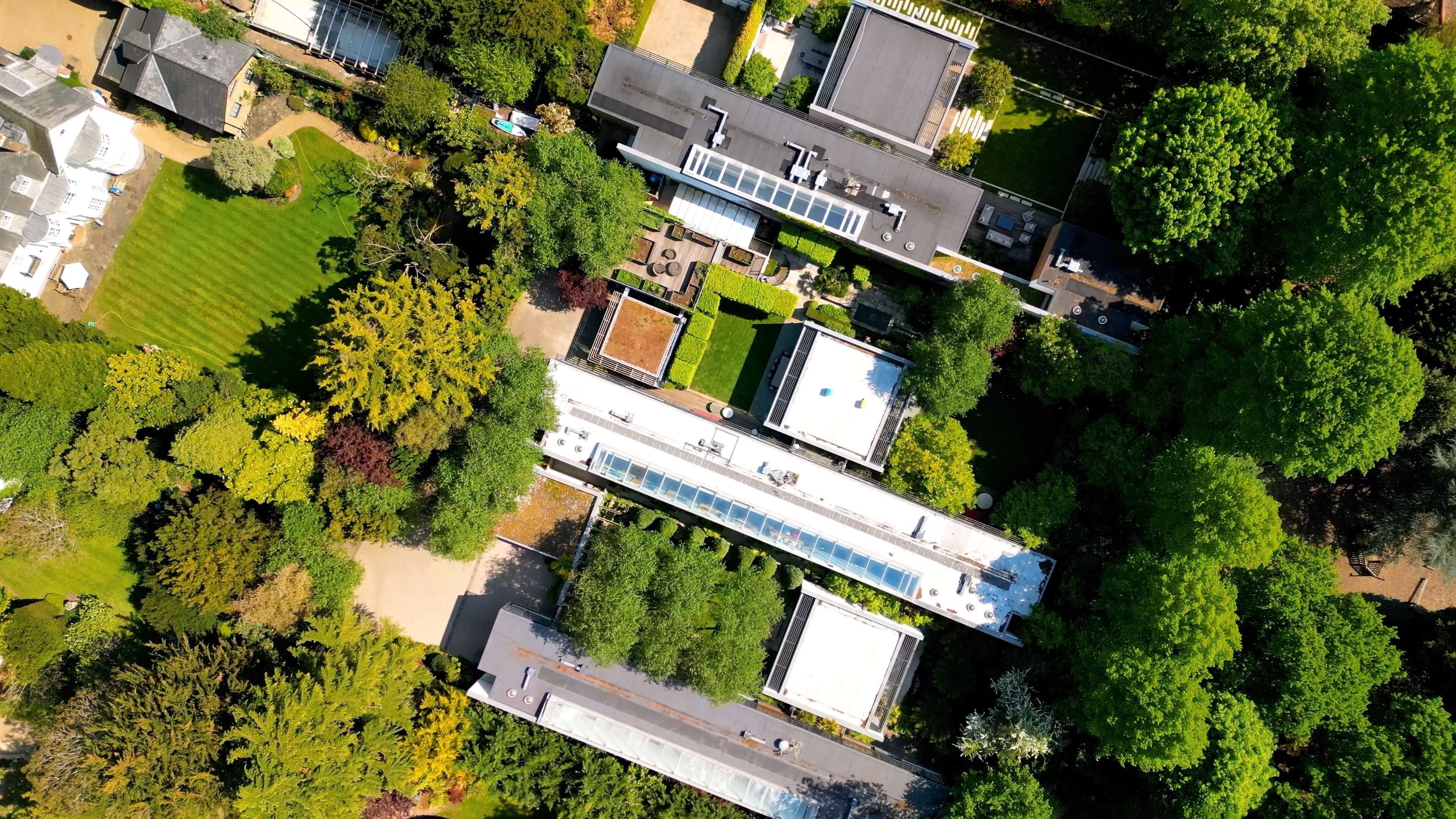 Aerial view of a modern house with flat roofs surrounded by dense green trees and lawns.