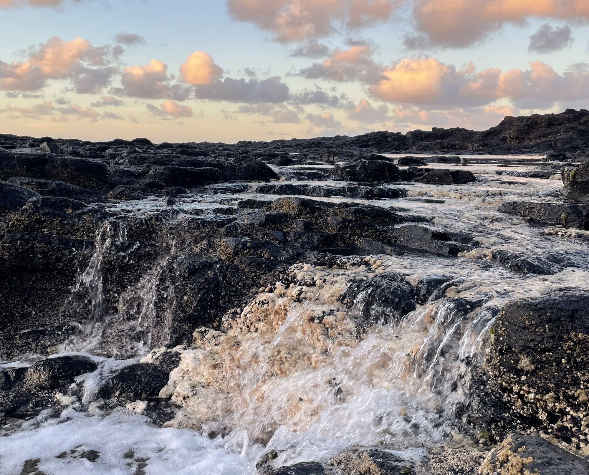 Rock pools and a low waterfall catching a gold and pink sunrise