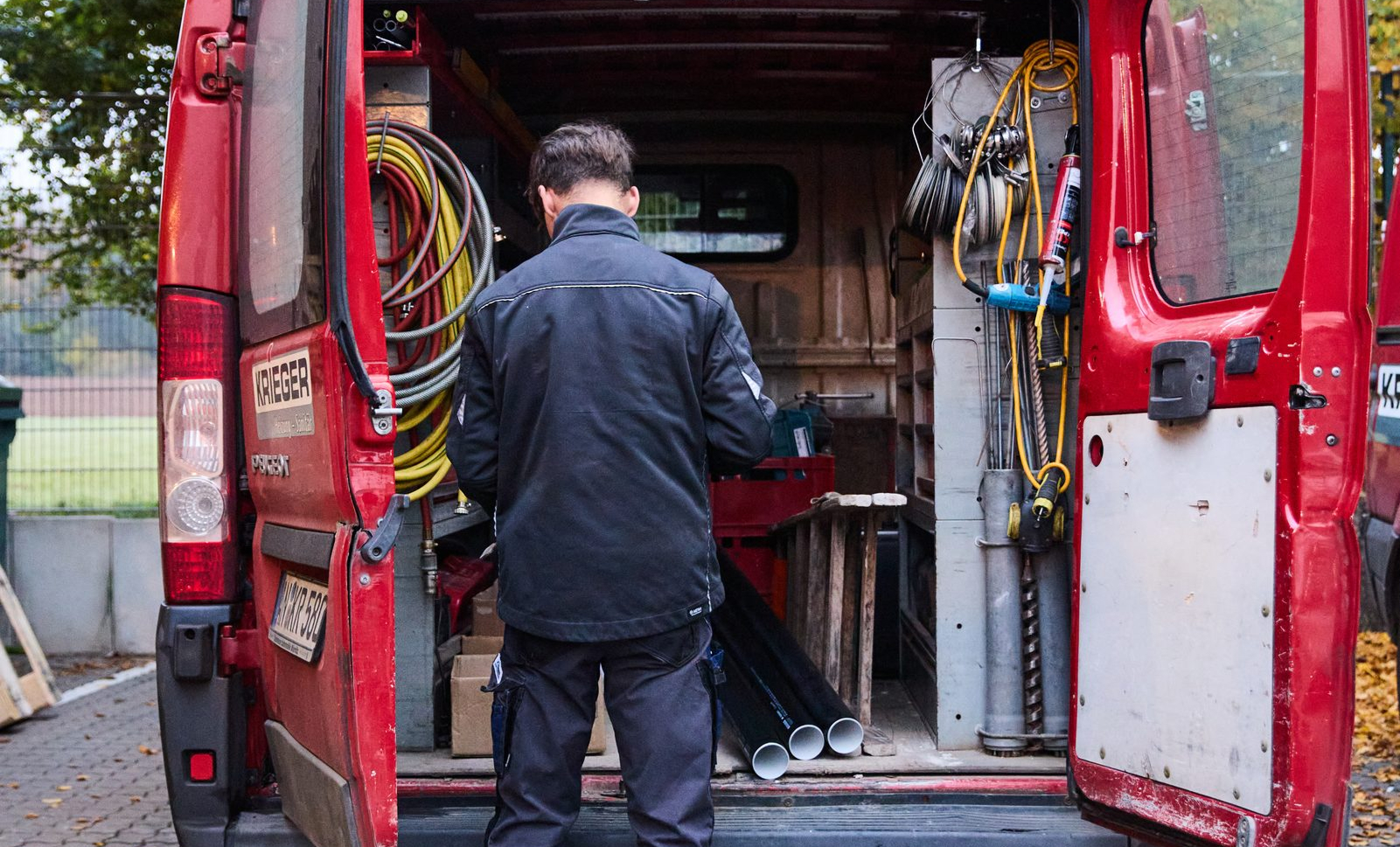 Fünf Handwerkerinnen und Handwerker in Arbeitskleidung gehen gemeinsam mit Werkzeugen aus einer Werkstatt.