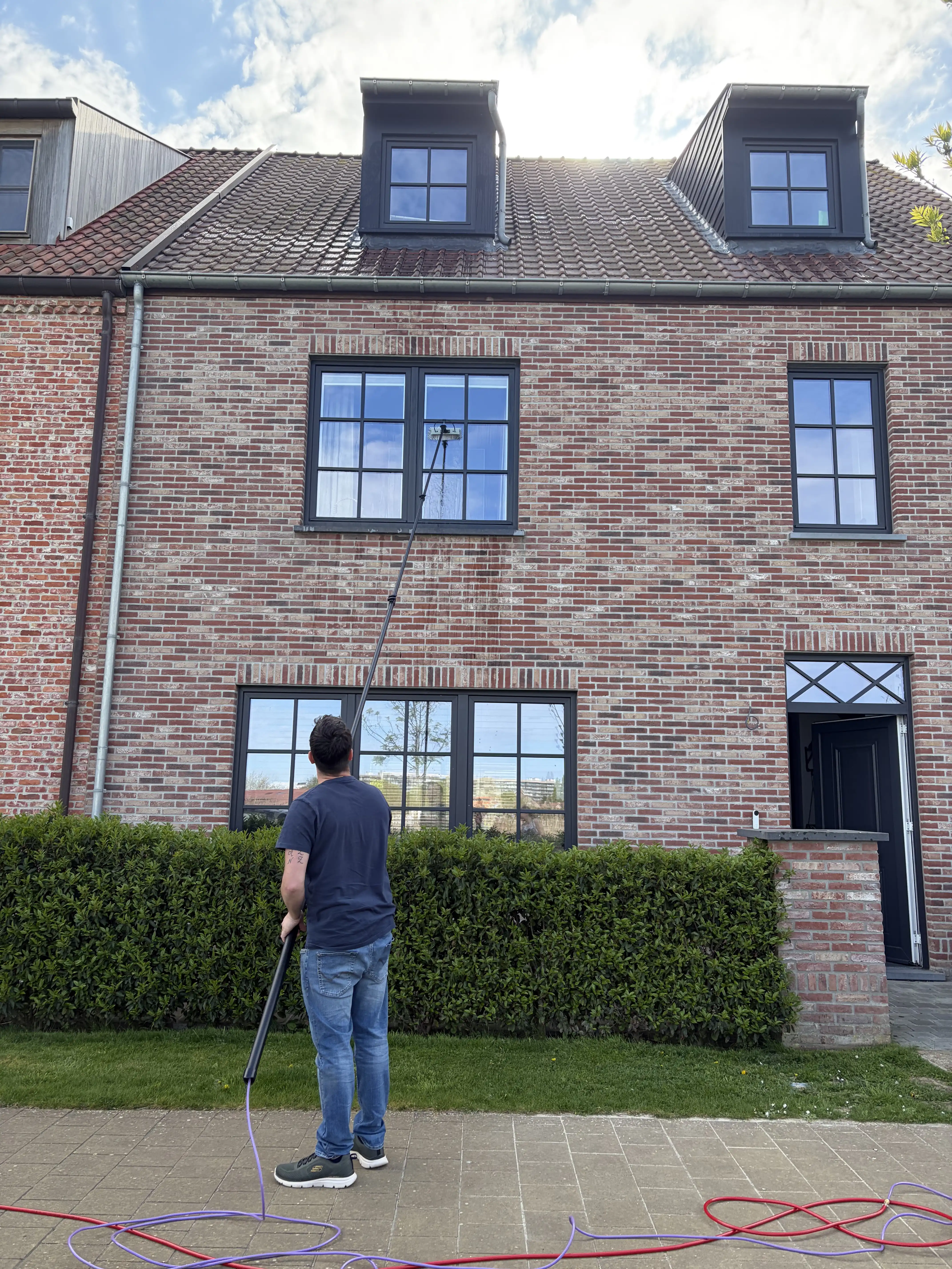 Kenneth wast de ramen van een woning met een telescoopsteel