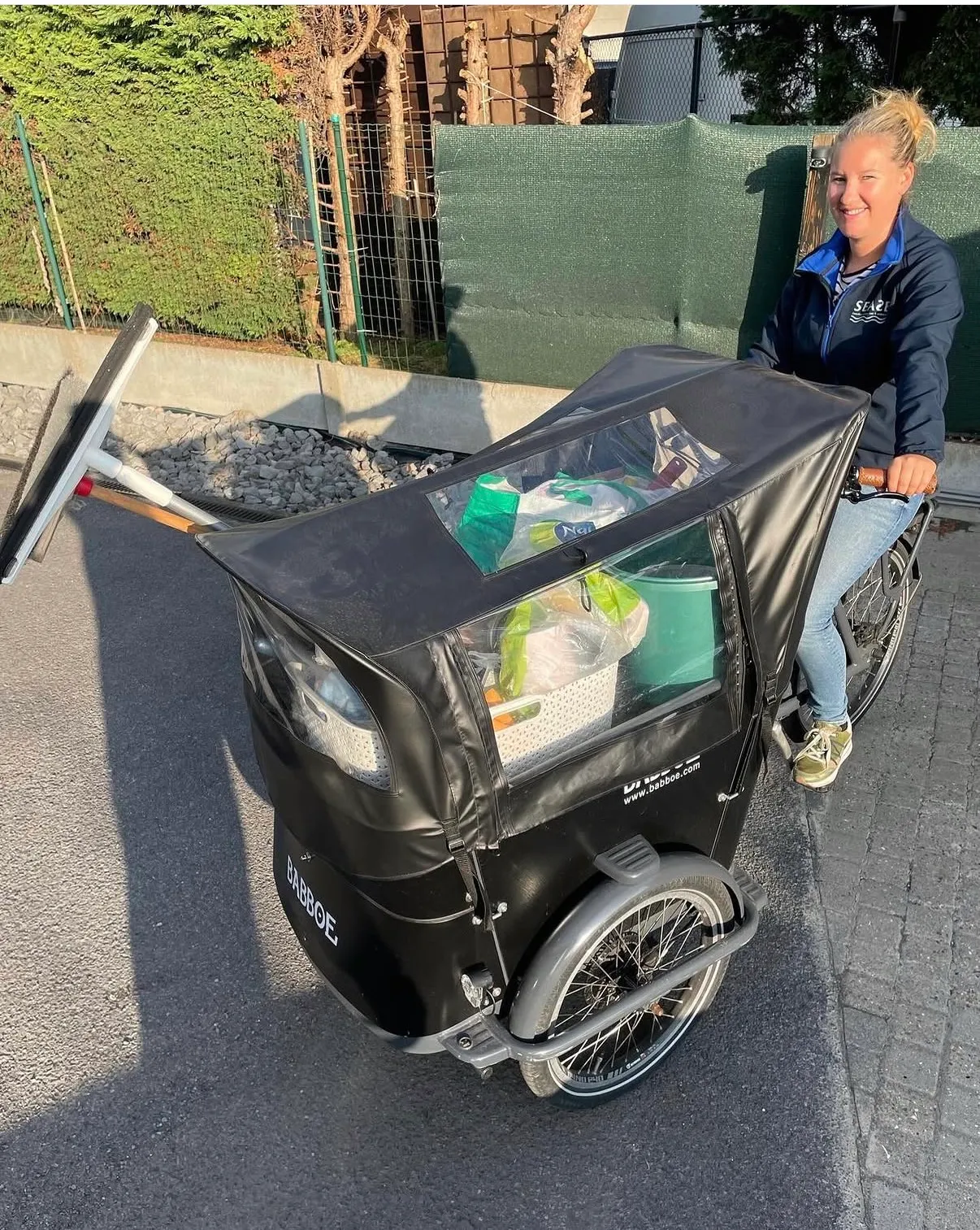 Lynn op de fiets onderweg naar een opdracht, met haar schoonmaakmateriaal in de voorbak