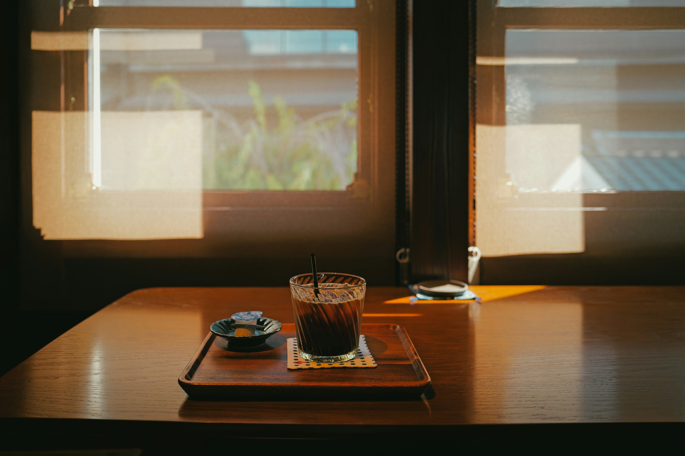 An iced coffee on a wooden tray by a sunlit café window