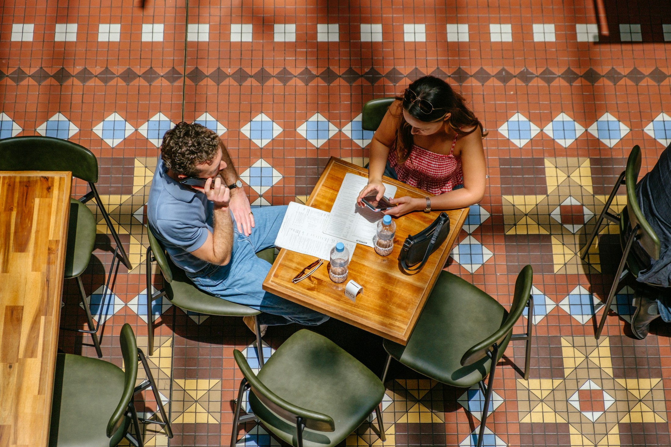 Two guests reading at a small wooden table on a patterned tiled floor, seen from above
