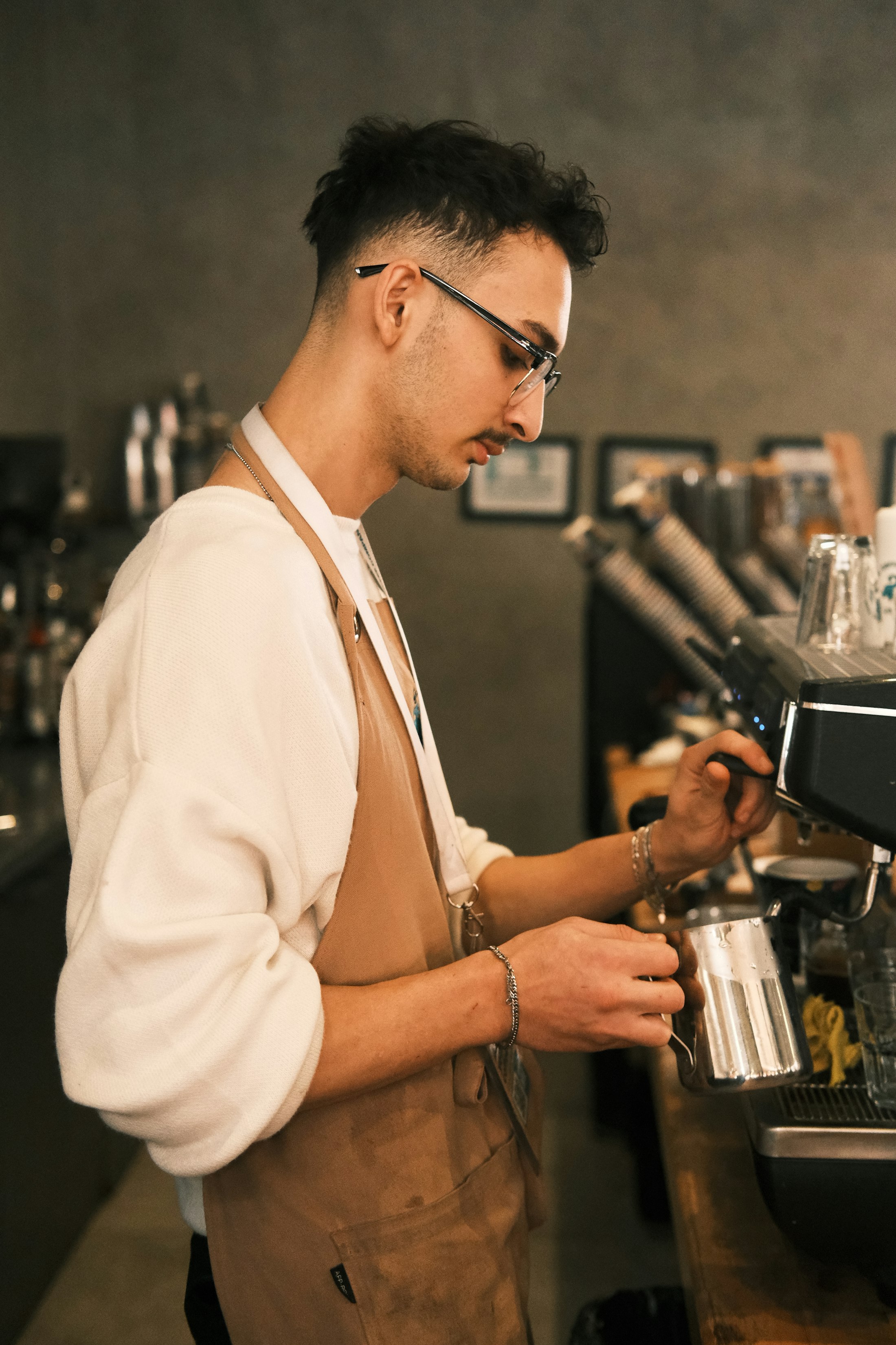 A barista in a linen apron steaming milk at the espresso machine
