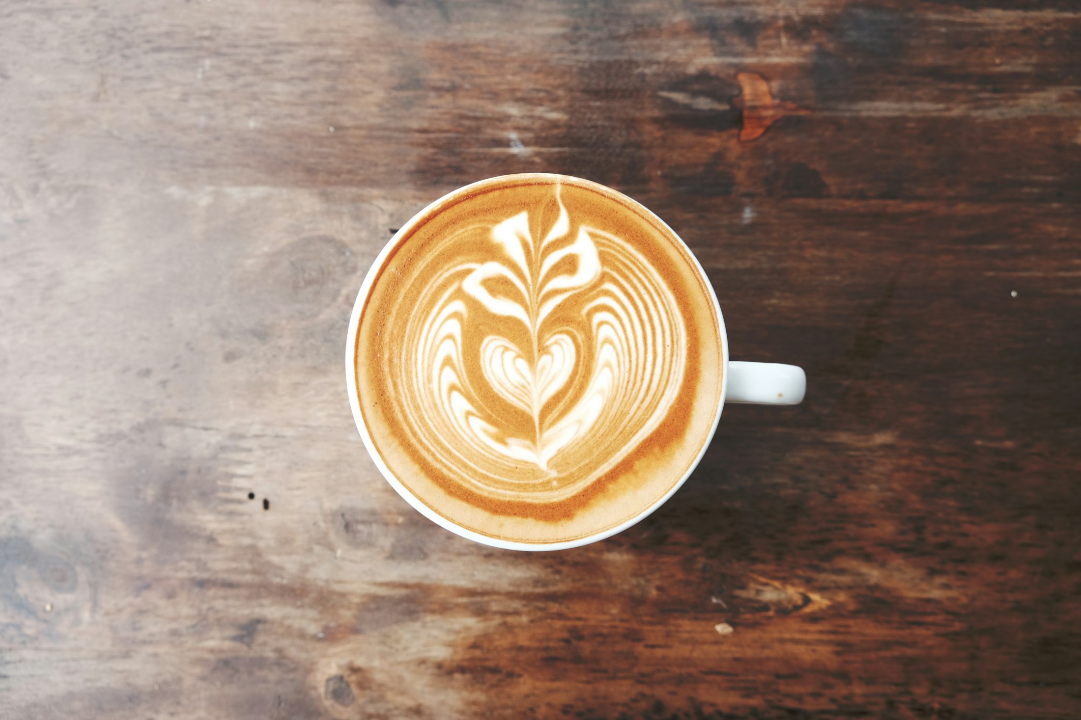 A flat white with rosetta latte art on a dark wooden table