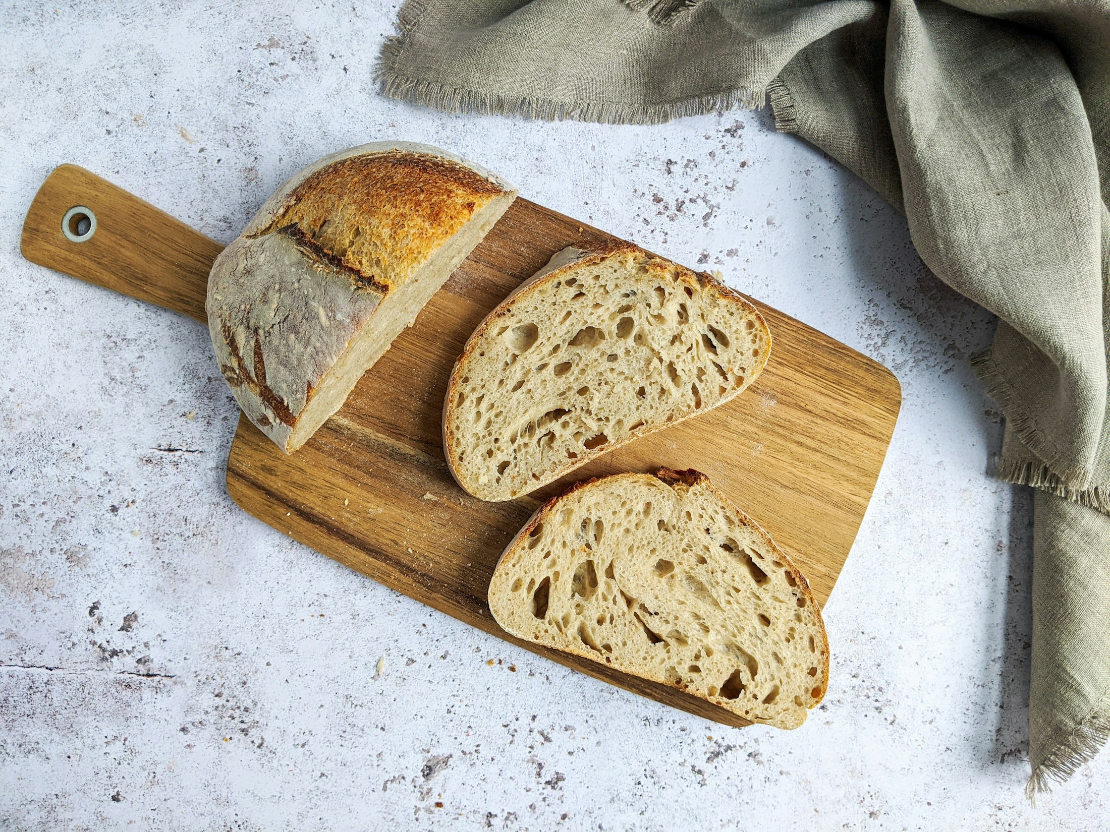 A sliced sourdough loaf on a wooden board with a linen cloth