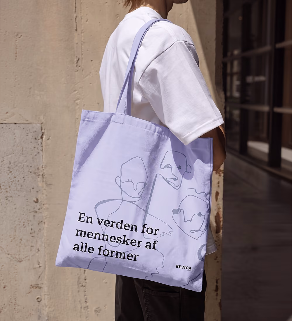 Lavender Bevica tote bag with line-drawn faces and the Danish message “En verden for mennesker af alle former.”