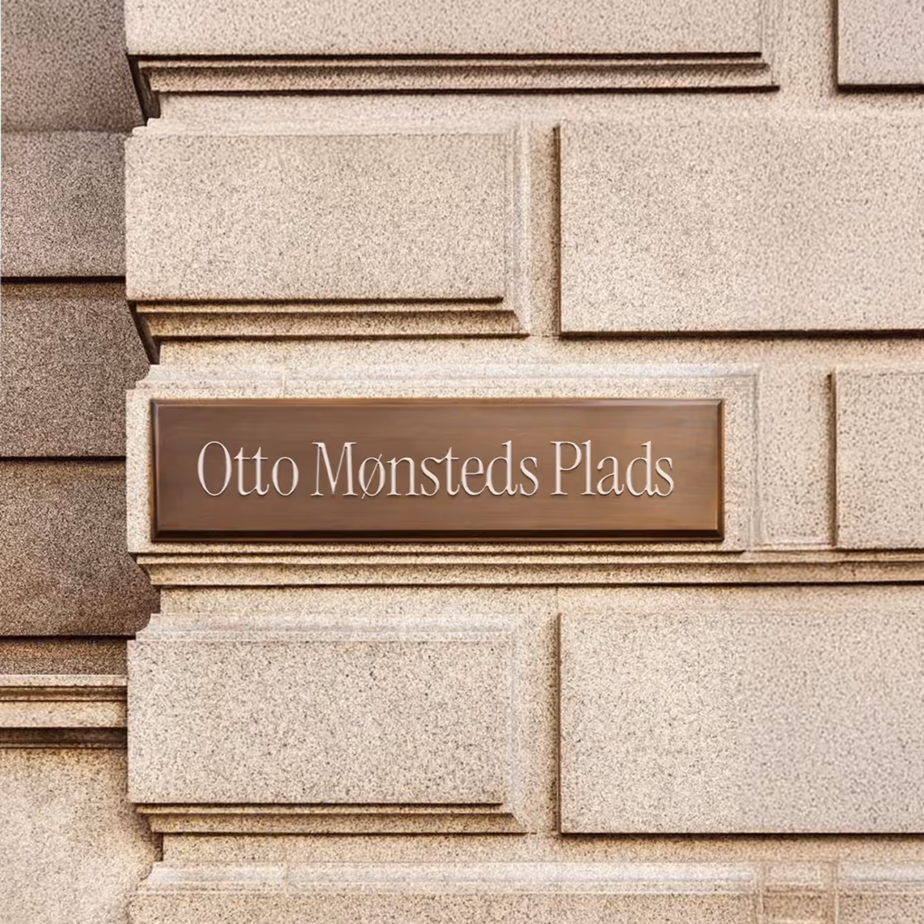 Otto Mønsteds Plads serif wordmark on a bronze-colored plaque mounted on a stone facade.