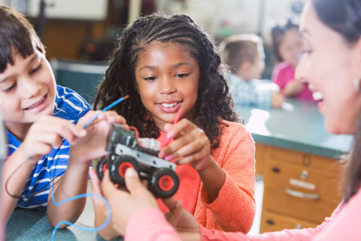 Children smiling while building an electric toy car together in a classroom STEM activity