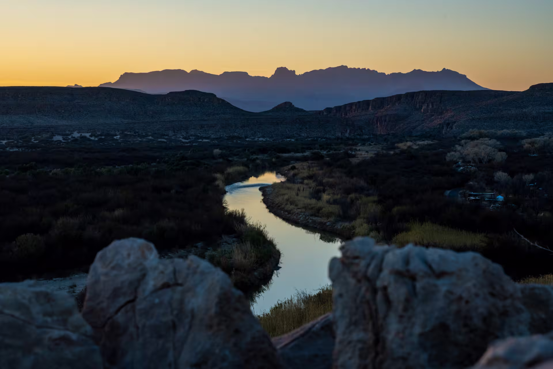 River winding through a desert canyon at golden hour with mountain silhouettes in the background