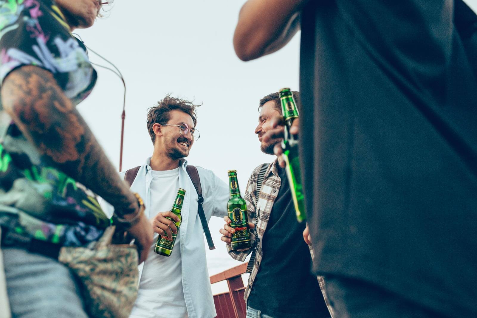Junge Männer stehen draußen, trinken Bier und unterhalten sich lächelnd.