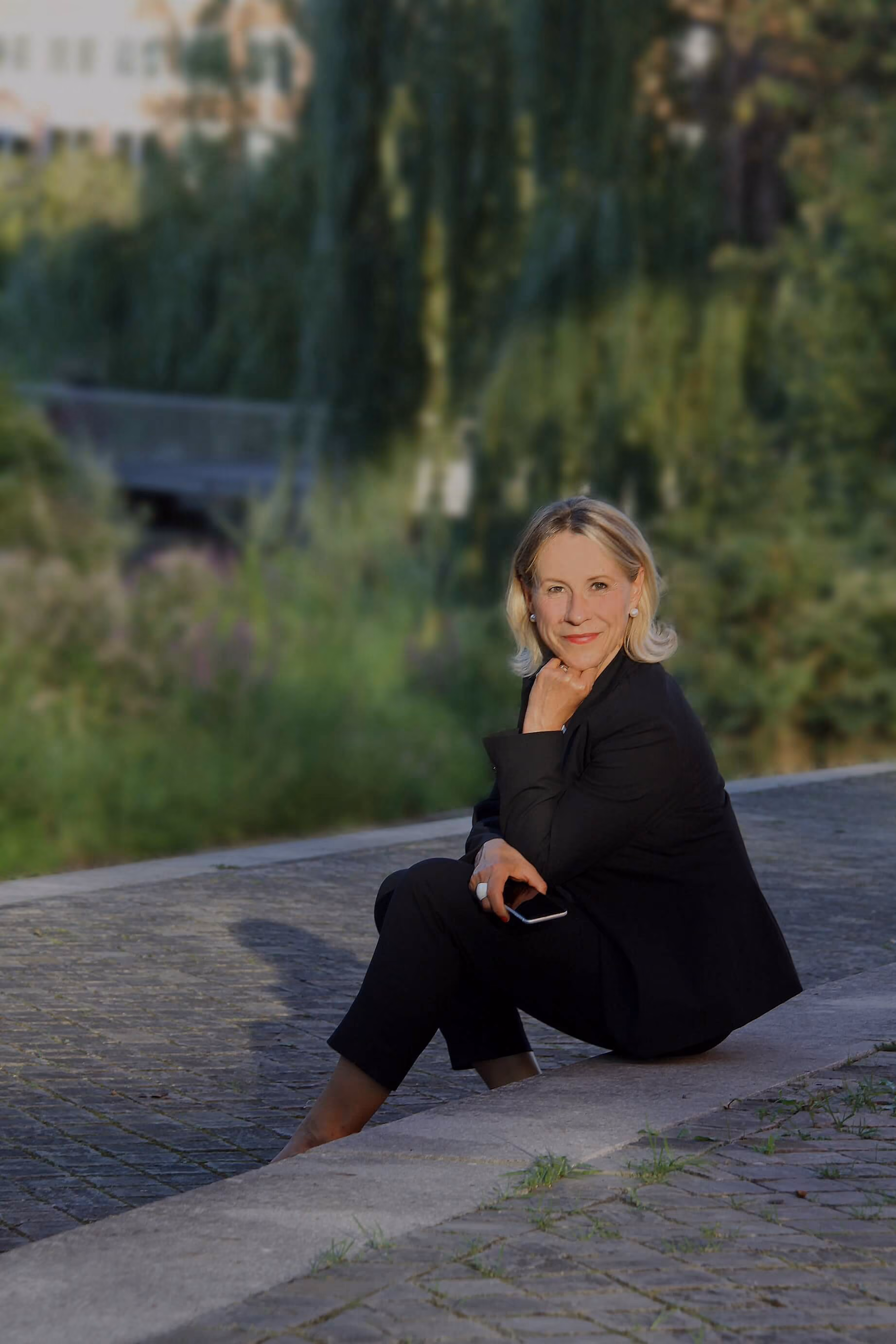 Anke Ruprecht sitzend im schwarzen Anzug im Freien mit Smartphone in der Hand – persönliche Begleiterin für besondere Erlebnisse als Perlentaucherin.