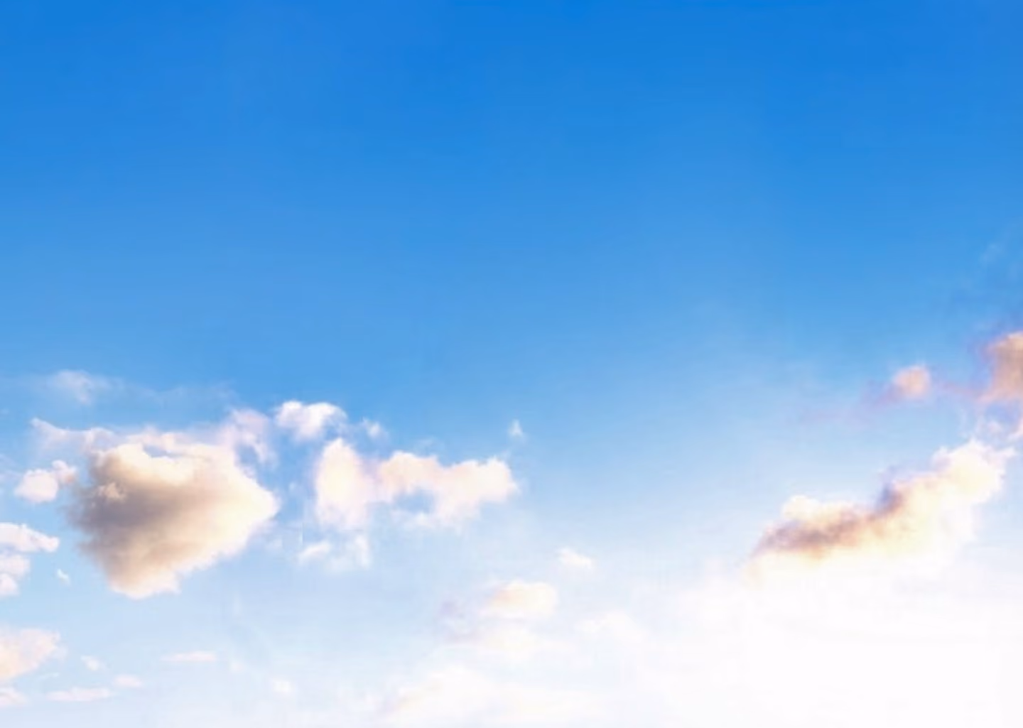 Blue sky with scattered white and light gray clouds illuminated by sunlight near the horizon.