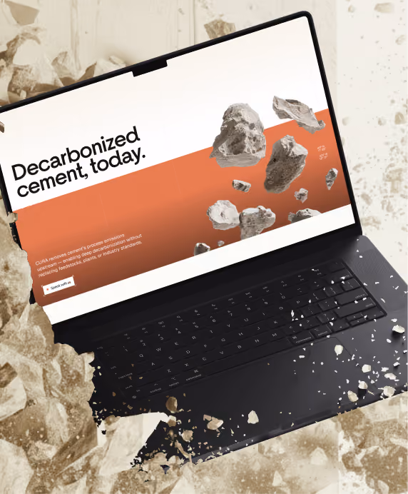 Black laptop with screen displaying the text 'Decarbonized cement, today.' Several floating gray cement rocks are shown on the screen and around the laptop, with a background of similar rocks in beige tones.