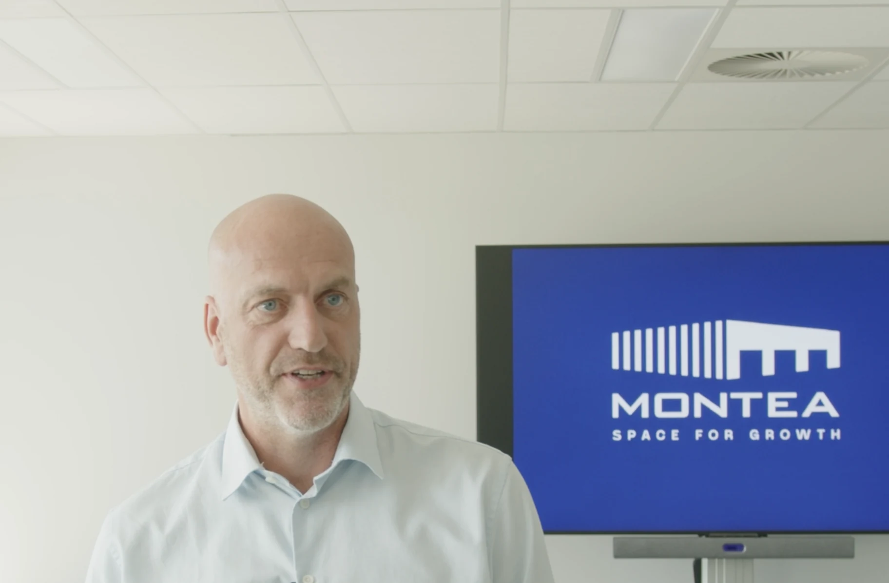 Dirk van Buggenhout of Montea speaking in a meeting room, with the Montea logo on the screen behind him