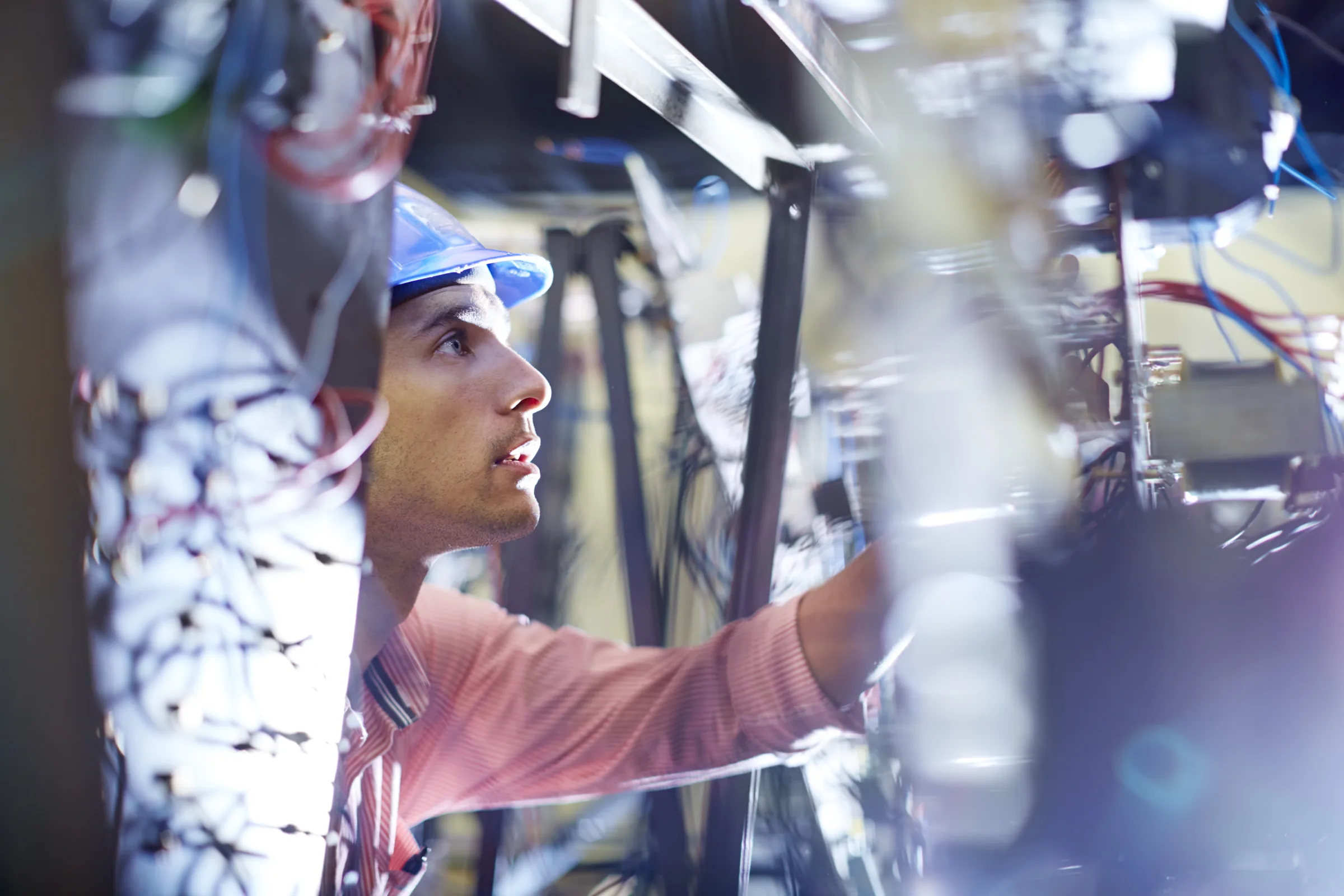 Technician in a hard hat inspecting electrical wiring and control equipment in a manufacturing plant