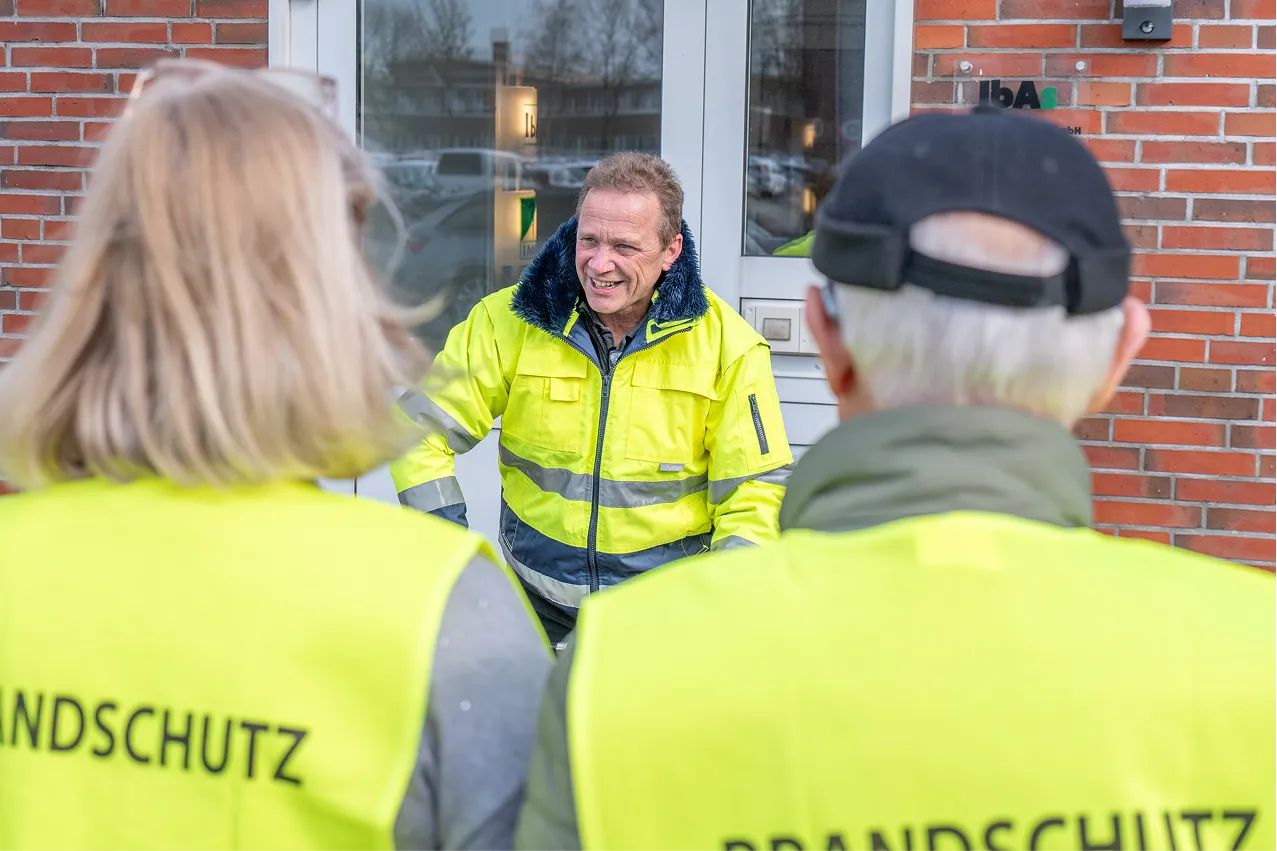 Gespräch mit Mitarbeitenden in Brandschutz-Warnwesten vor dem Betriebsgebäude