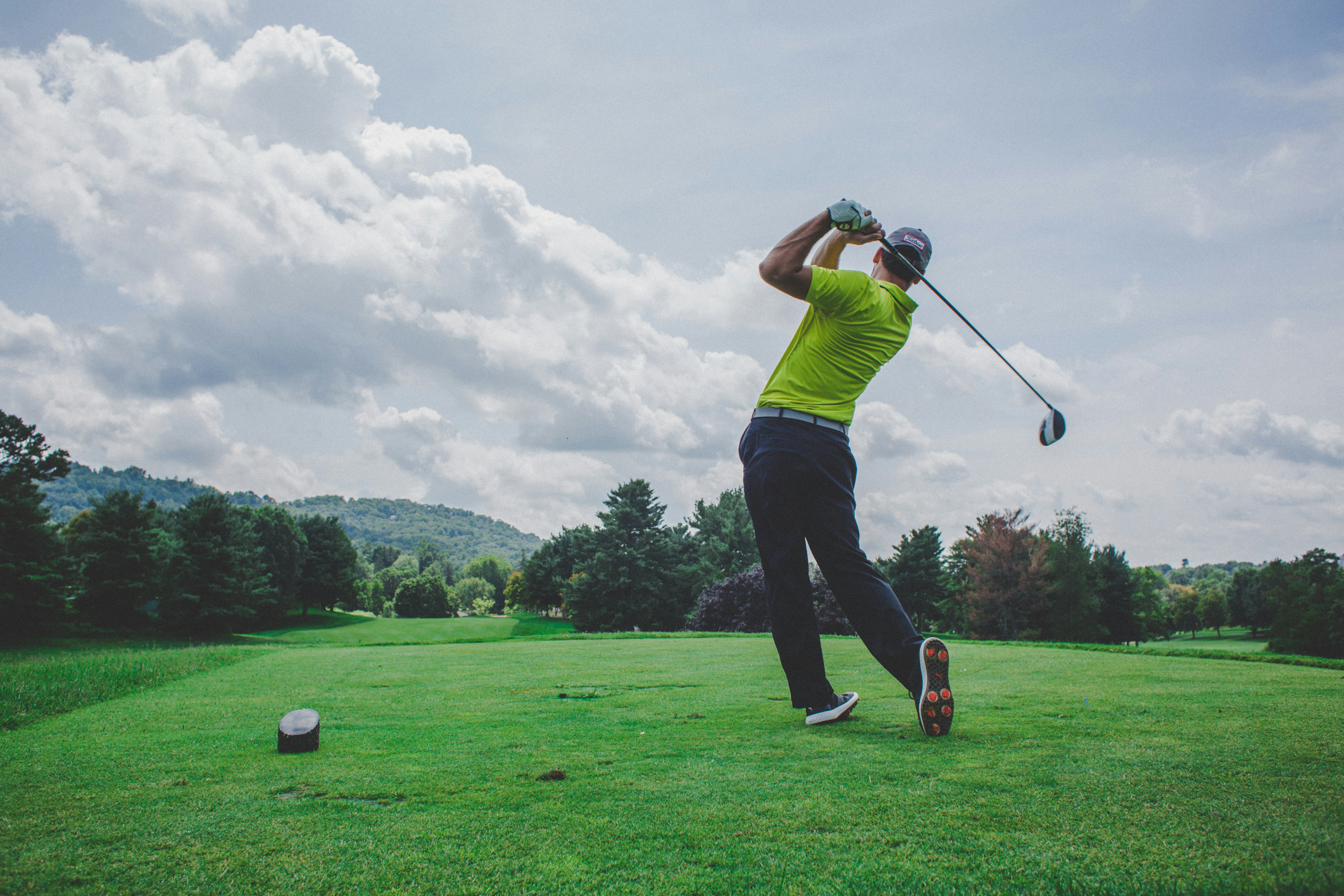 Golfer swinging club on a sunny golf course.