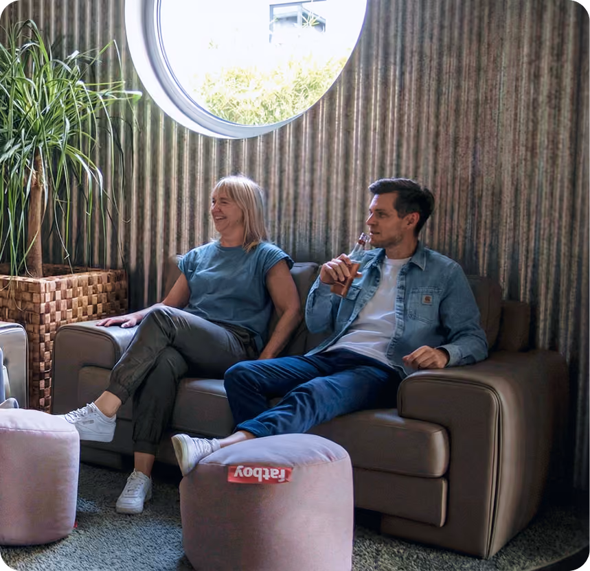 Zwei Kollegen im Gespräch auf einem Sofa im orgaMAX-Büro