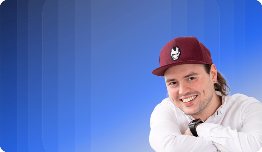 Junger Mann mit weißem Hemd und roter Kappe mit Iron-Man-Logo lächelt vor blauem Hintergrund.