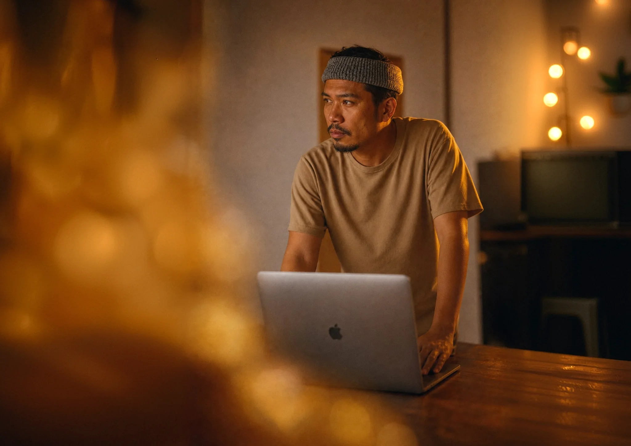 Man in a knitted beanie leaning over a laptop in a warmly lit room