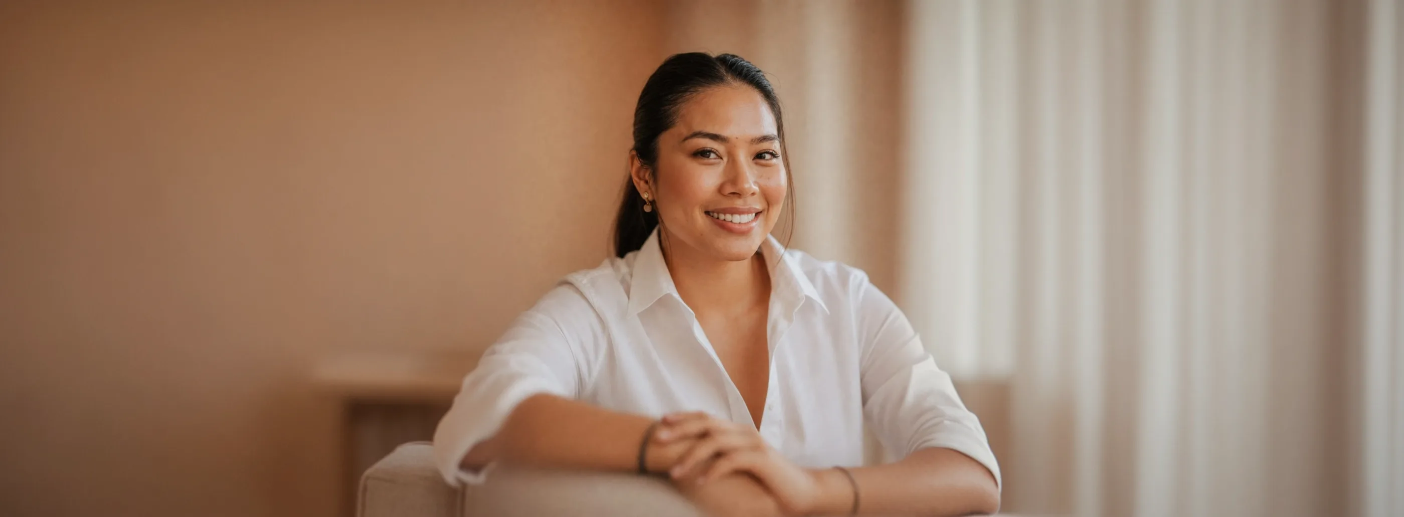 Smiling woman in a white shirt seated in a warm-toned room
