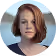 Portrait of a woman with short reddish hair wearing a black top, looking slightly to the side against a soft blue background.
