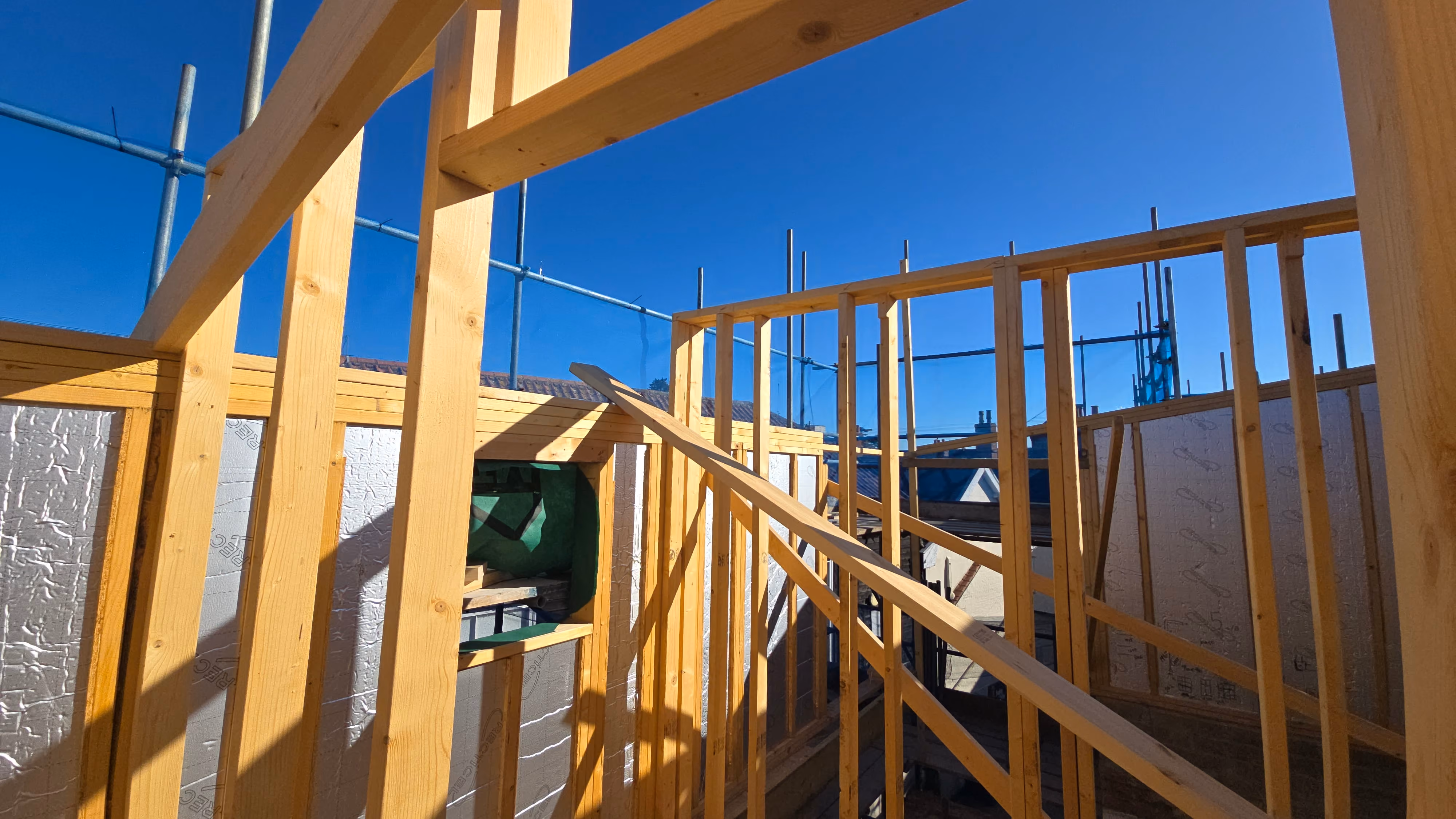 Wooden framing structure of a building under construction with a clear blue sky in the background.