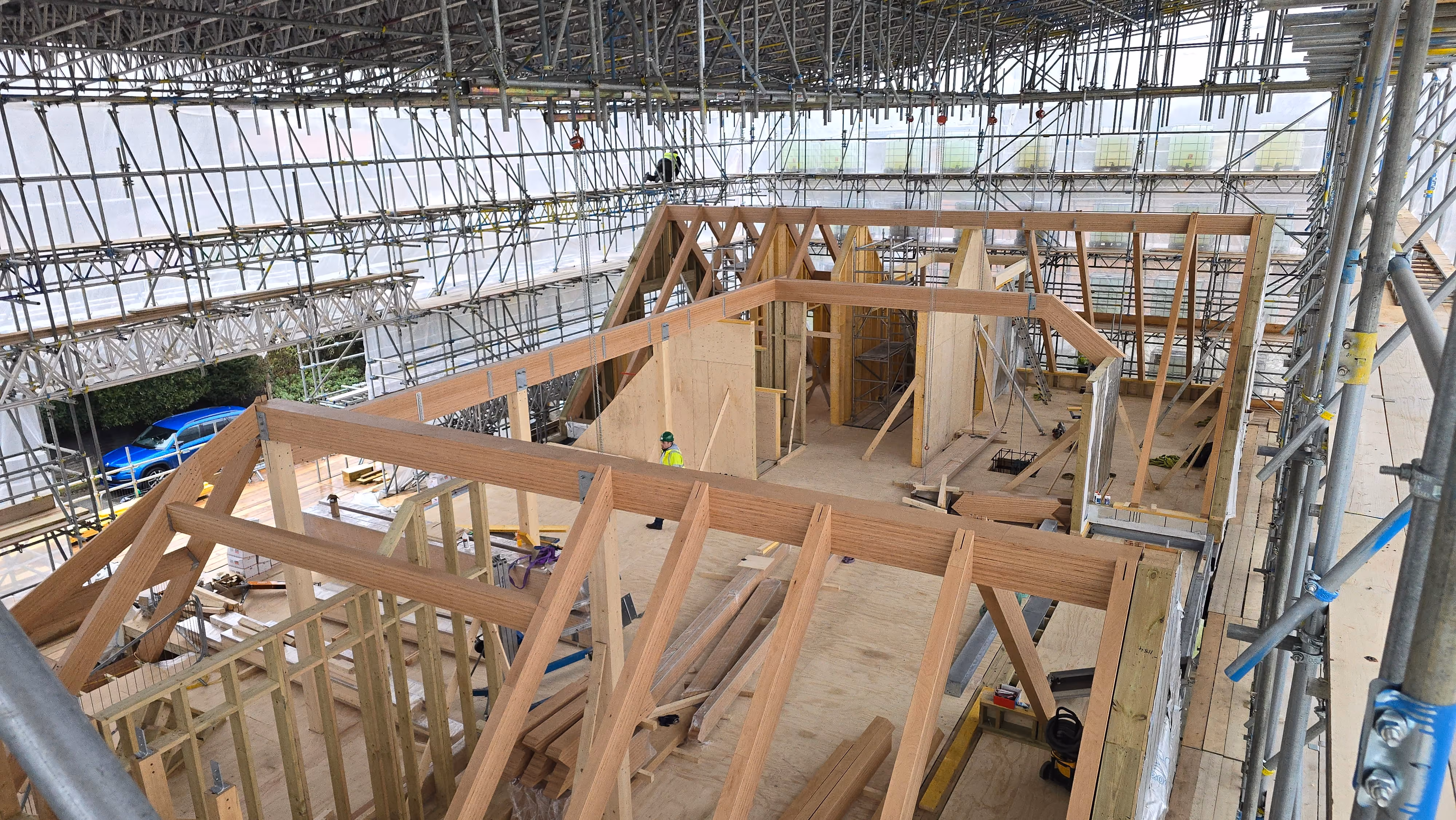 Indoor wooden framework of a building under construction with scaffolding and workers wearing safety gear.
