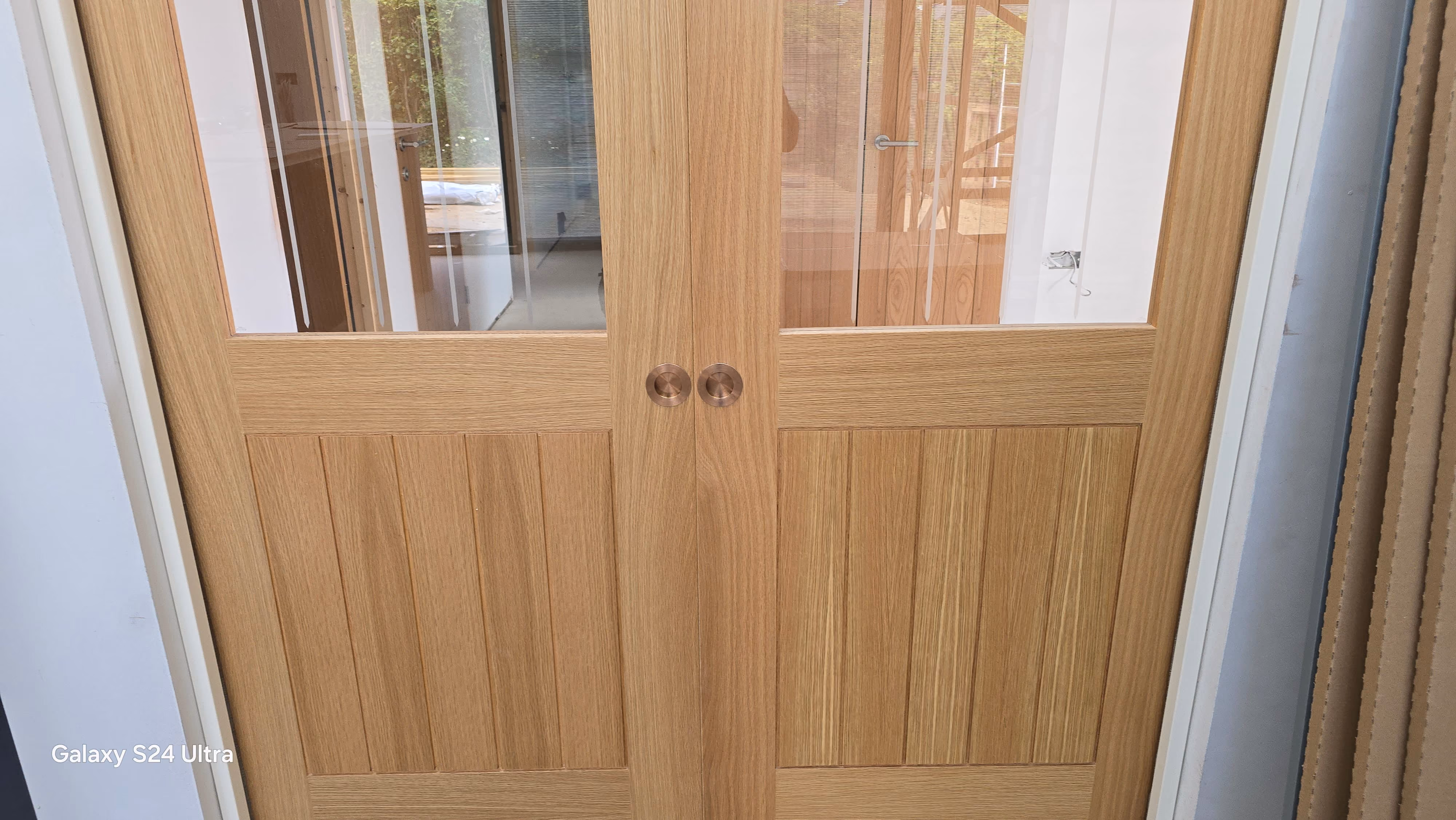 Double wooden doors with glass panels on top and vertical wood paneling on the bottom, reflecting an indoor space behind them.