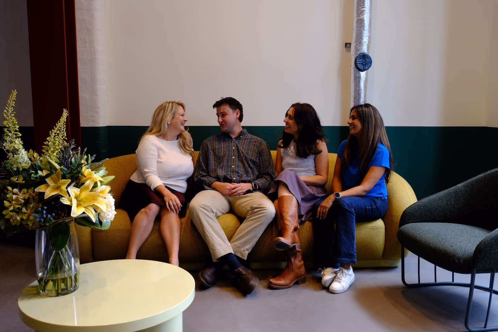 Ghania and Gemma sitting and chatting on a yellow couch with clients
